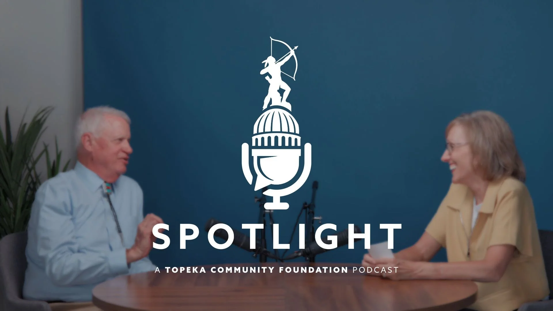 Hurst Coffman and Marsha Pope sit at a round table talking to each other. The Spotlight podcast logo is centered on the photo.