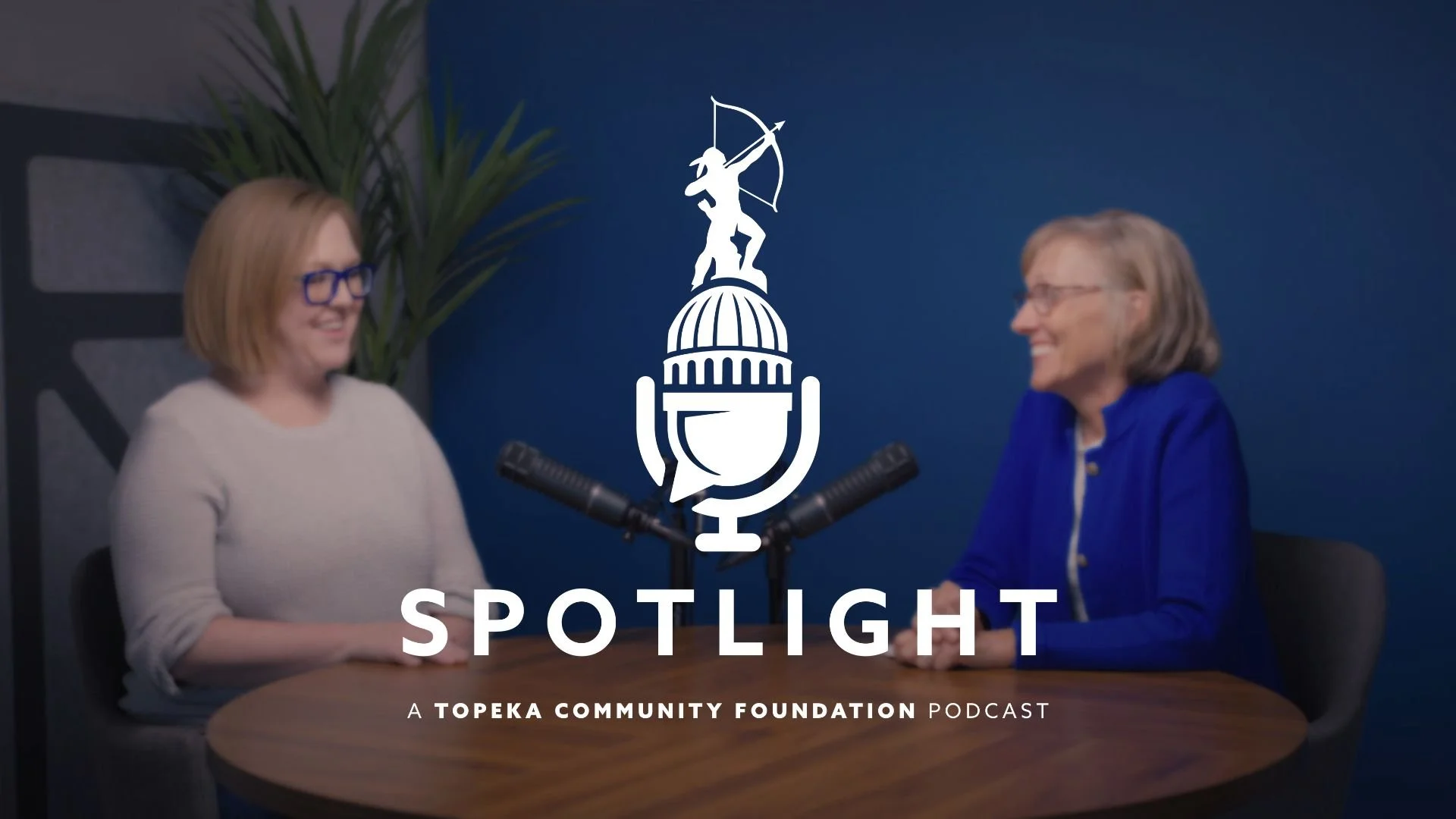 Marsha Pope and Janice Watkins sit at a table talking to each other. The Spotlight podcast logo is centered in the photo.
