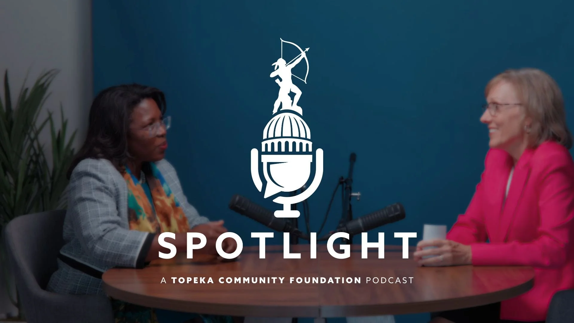 Dr. Tiffany Anderson and Marsha Pope sit at a table talking to each other. The Spotlight podcast logo is centered on the photo.