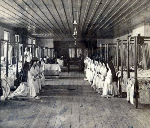 « Quartier Vieux-Québec - Côte du Palais - Hôtel-Dieu. Vue de l'intérieur, chambre des malades avec la présence de l'aumonier et des religieuses » (Bibliothèque et Archives nationales du Québec).