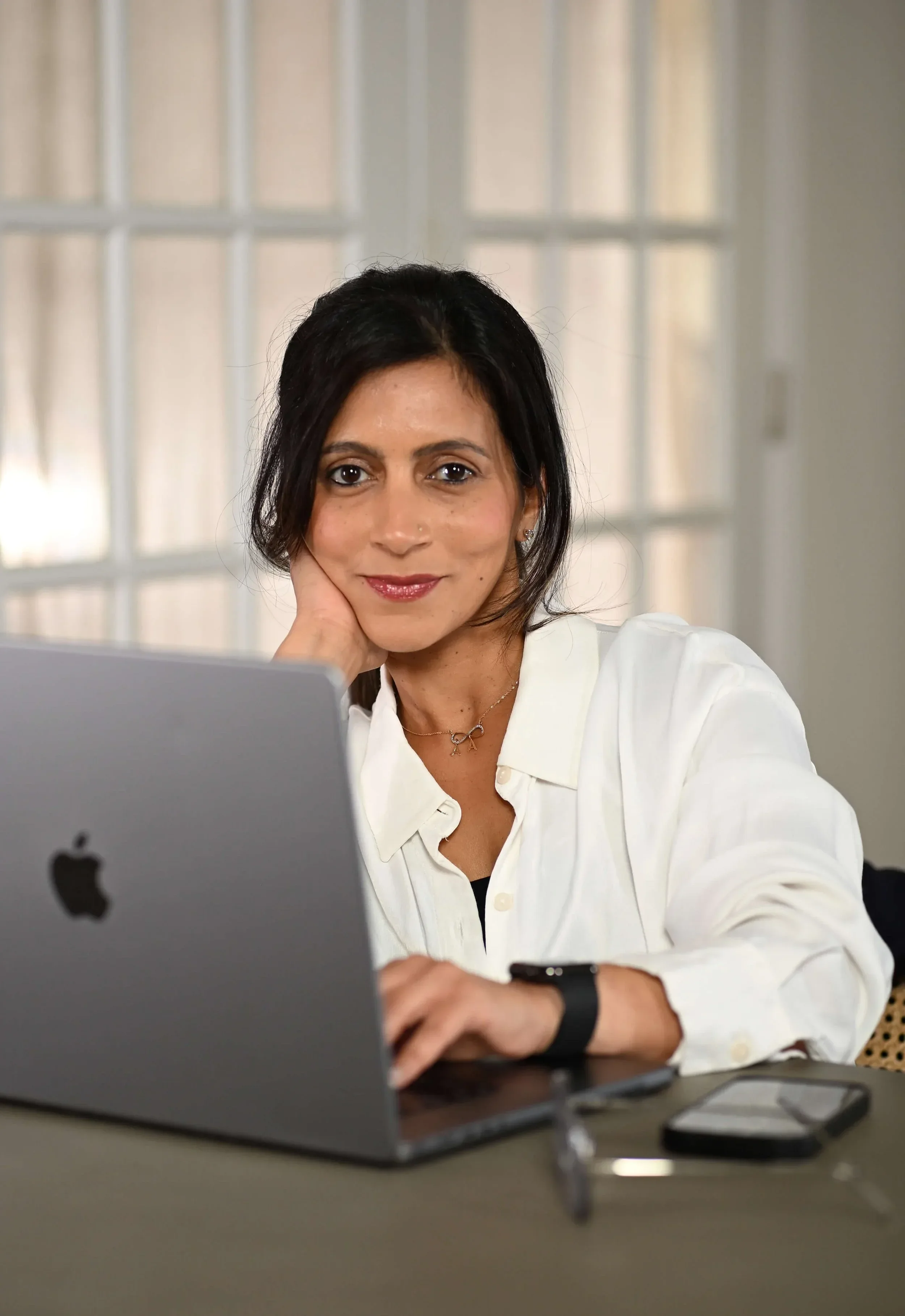 Mansi Narang, executive coach and founder of BrightHer consulting, smiling confidently at her desk while working on a laptop.