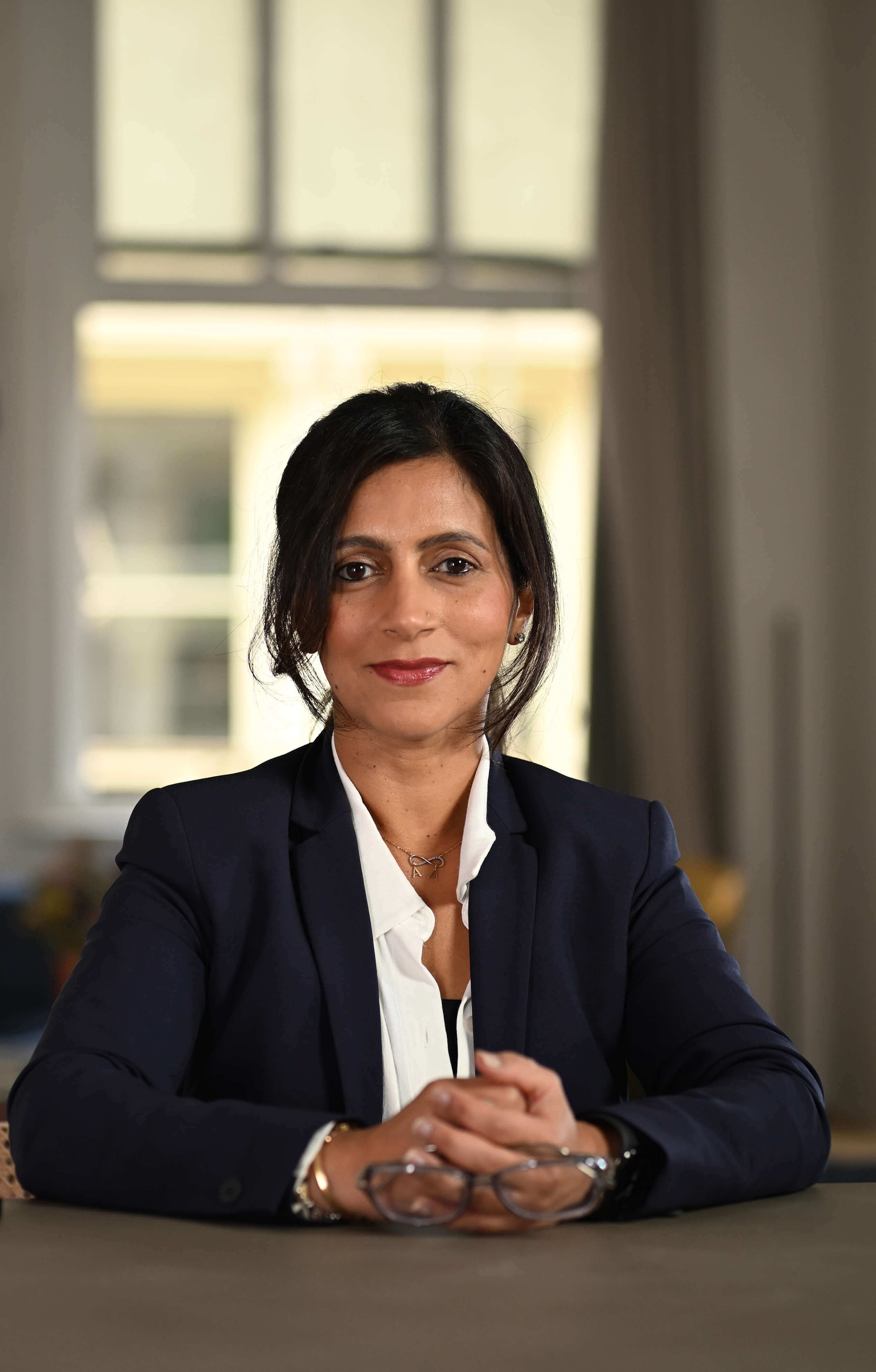 Mansi Narang at desk in a blazer holding glasses