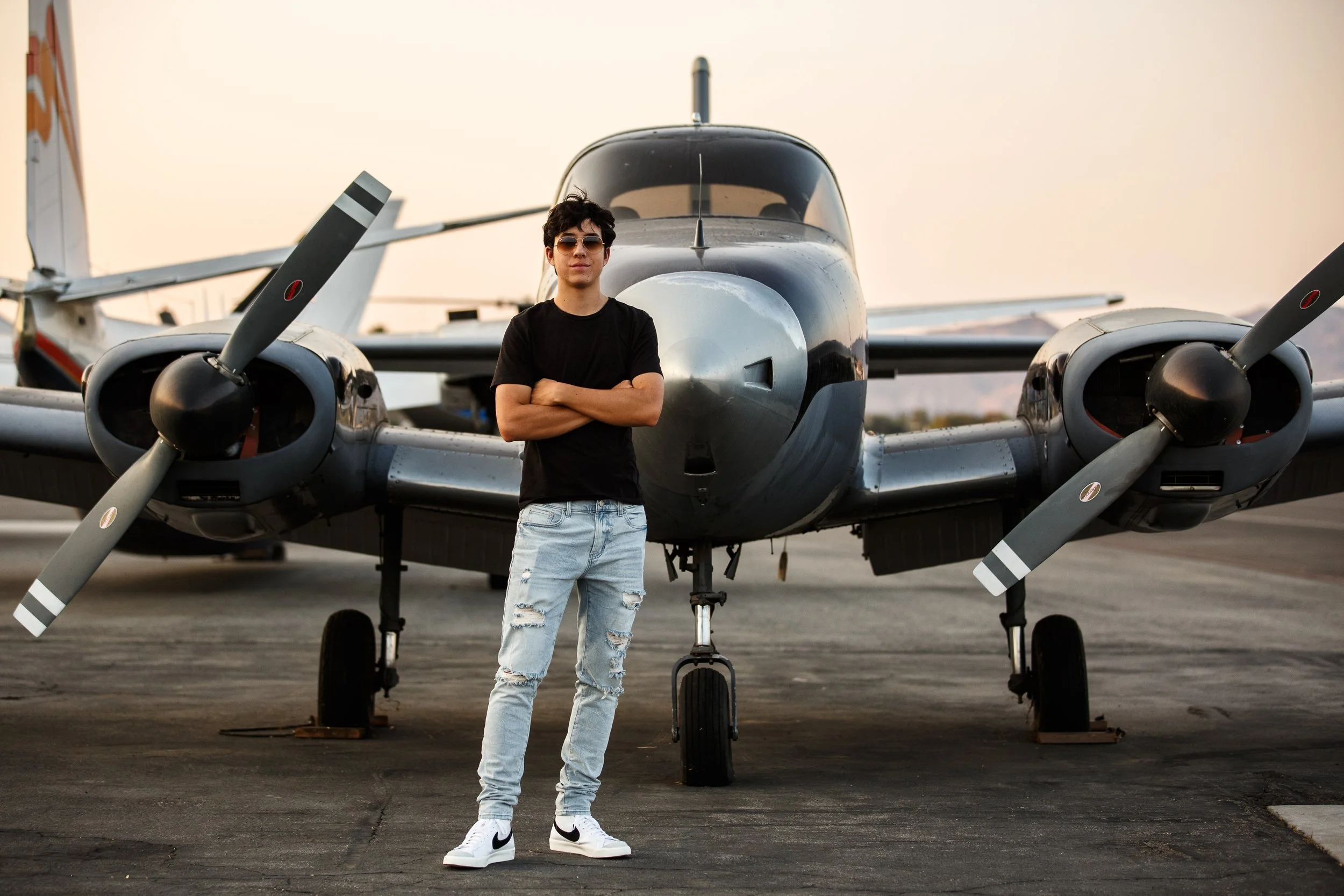 High school senior guy stands in front of a airplane with arms crossed because he is going to flight school after graduation.