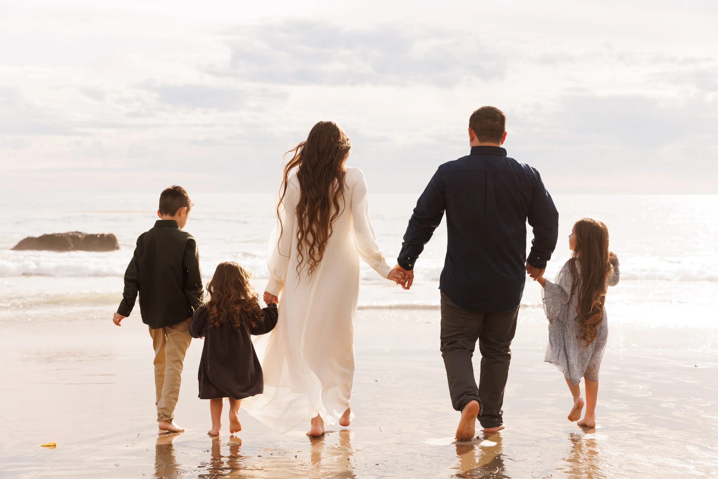 Golden hour at the beach, family walking towards the water together holding hands.