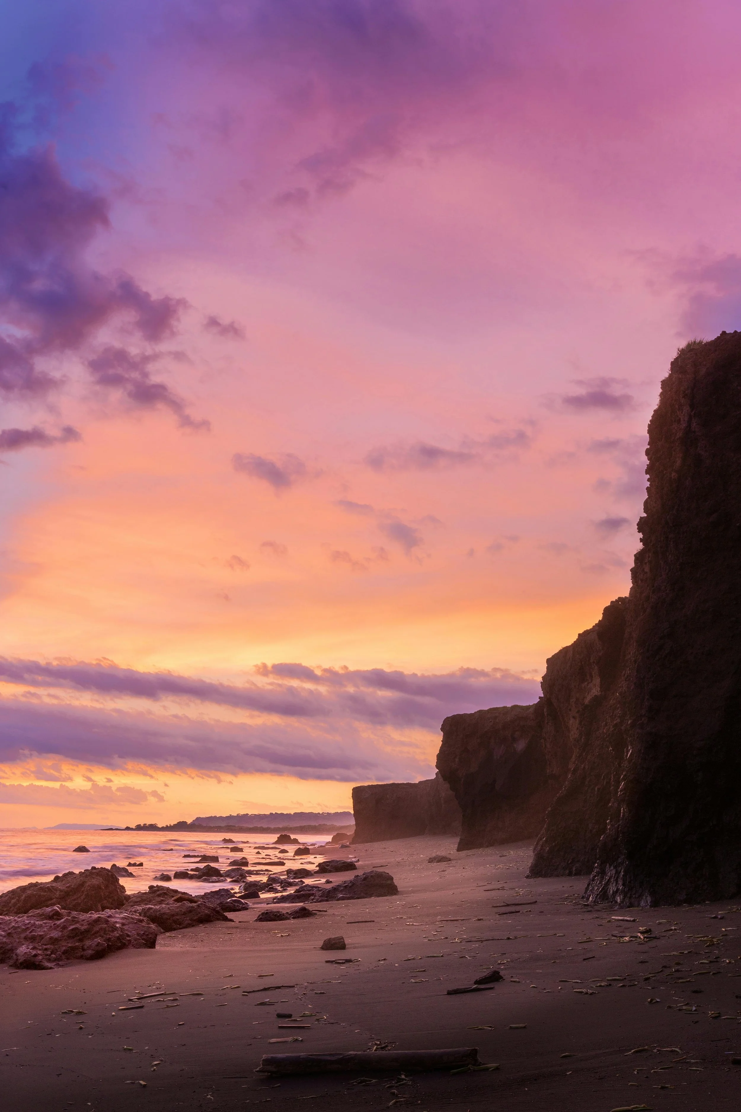 La mer à gauche, la plage au centre et des falaises sur la droite. Un soleil couchant et un ciel rose avec des nuages.