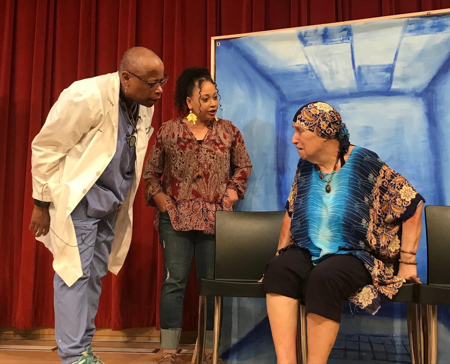 Image shows a Theatre of the Oppressed training scene where actors portray a doctor and social worker struggling to help a homeless woman who is in pain but is being percieved as a "difficult patient".