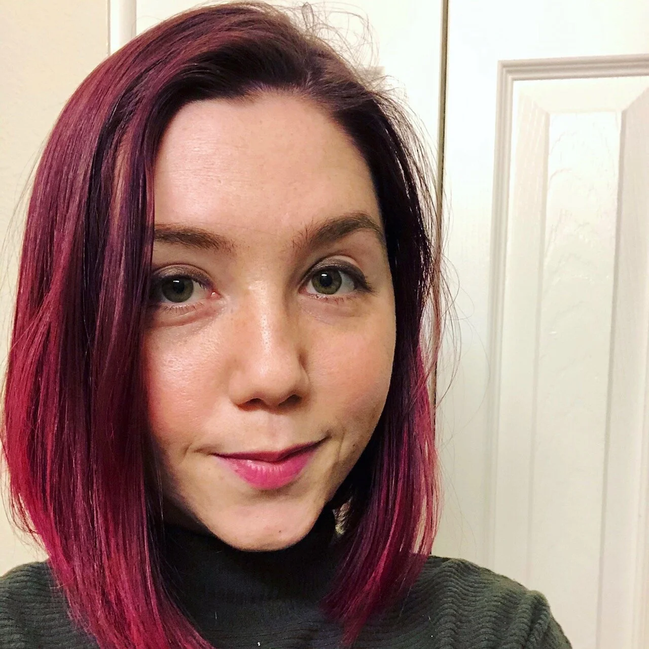 Maddi Porter, a white woman with straight pink hair, looks at you. She is wearing a dark turtleneck.