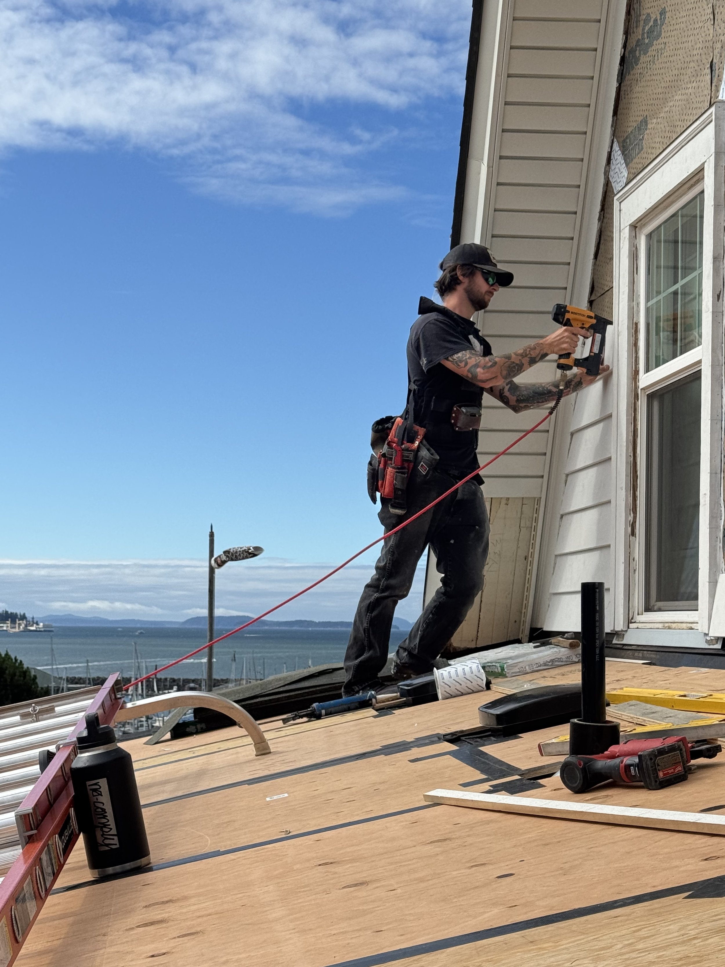 Man nailing on siding on top of a roof with the islands in the background