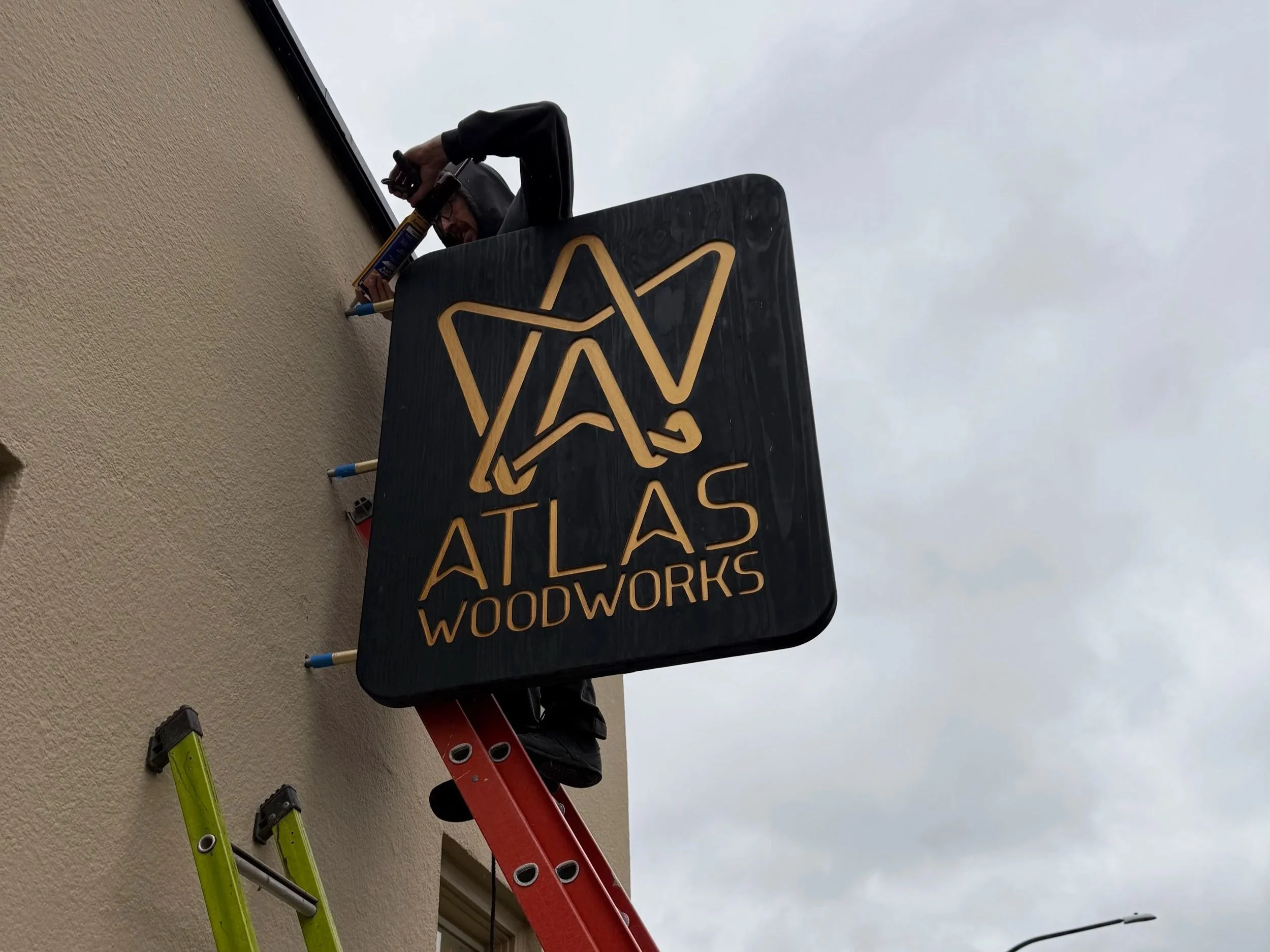 Man installing "Atlas Woodworks" Sign to building