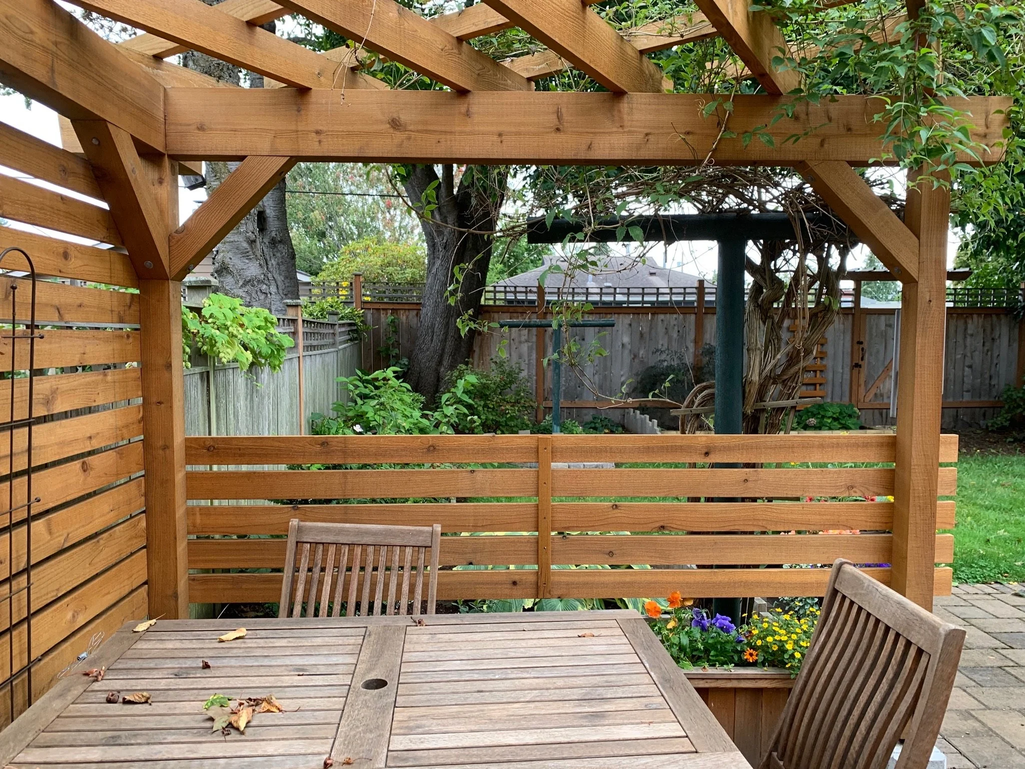 Cedar pergola sheltering a patio with a wood dining table and chairs, bordered by a horizontal slat fence.