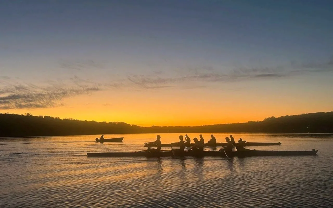 2 4s rowing boat in a lake with a sunrise.