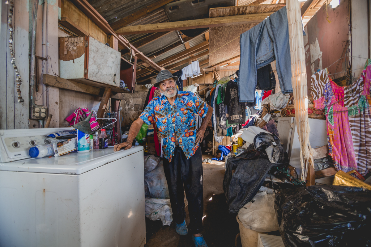 José Vazquez (78), in what is left of his home in San Lorenzo, Puerto Rico. When it rains, water seeps through their patched roof into their salvaged furniture as well as the donated, hung clothes. Everything is constantly wet and full of mold. As a result, José states he has developed pneumonia. He was strongly advised by his doctor to stay home, as he would be in even greater danger if he remained in the hospital due to the large amounts of virus cases within the facility. December 27, 2017.