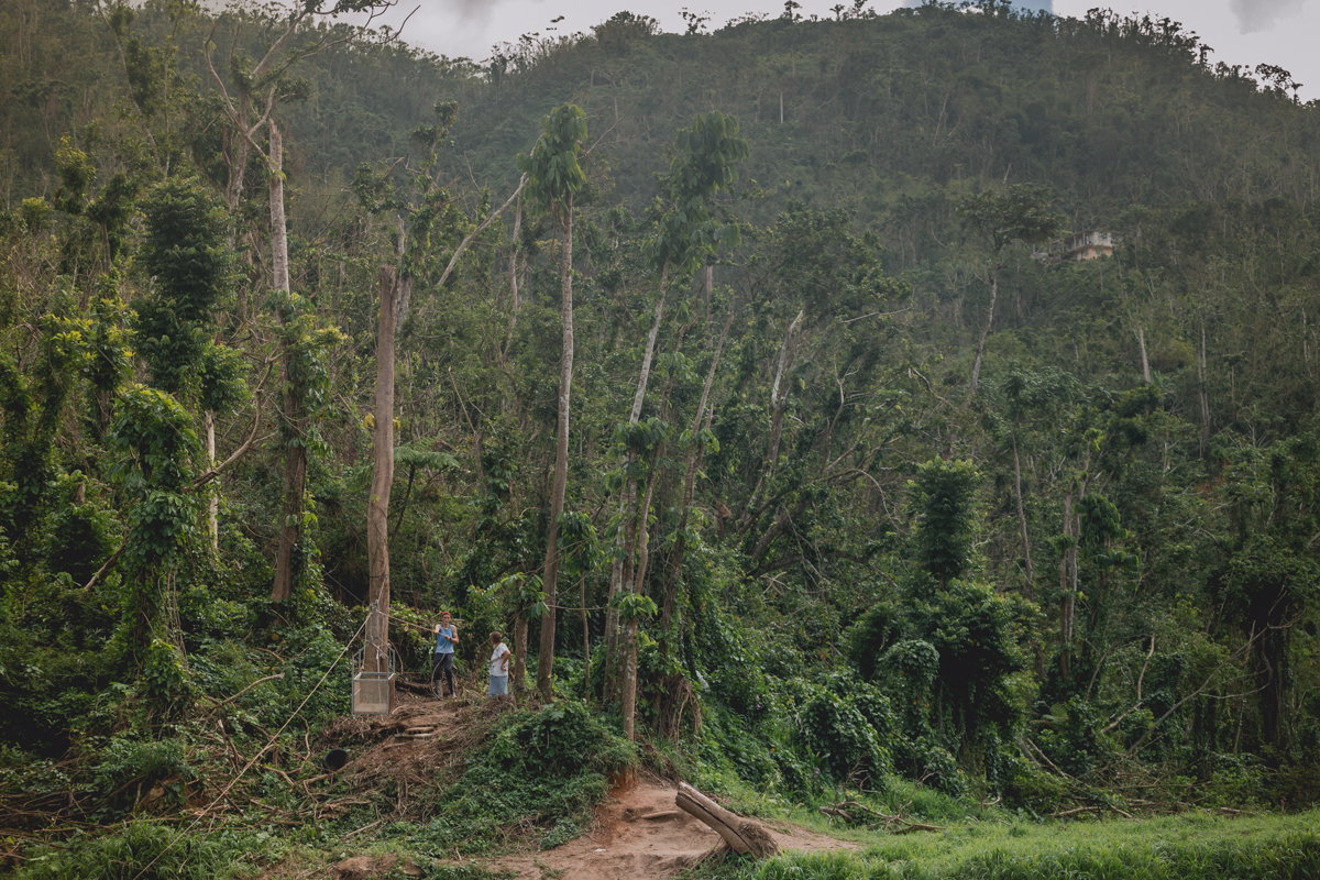 Zoraida (48) and Cristian (15) Sotomayor, checking their smartphones in the only place they have two bars of cell service without having to cross the river into town. Currently, they have to drive or hike down a long trail from their home to reach the river bank instead of taking the usual road to town. Utuado, Puerto Rico. December 28, 2017.