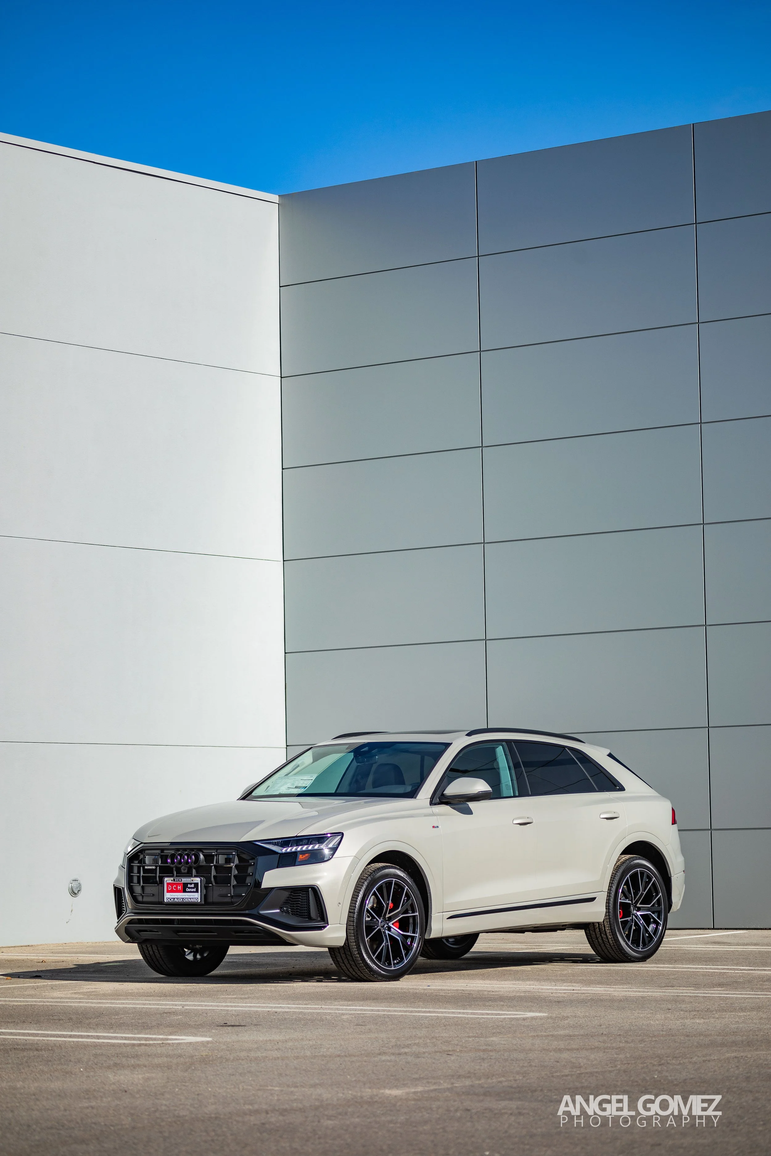 White SUV parked in front of a modern building with white and gray panels under a clear blue sky.