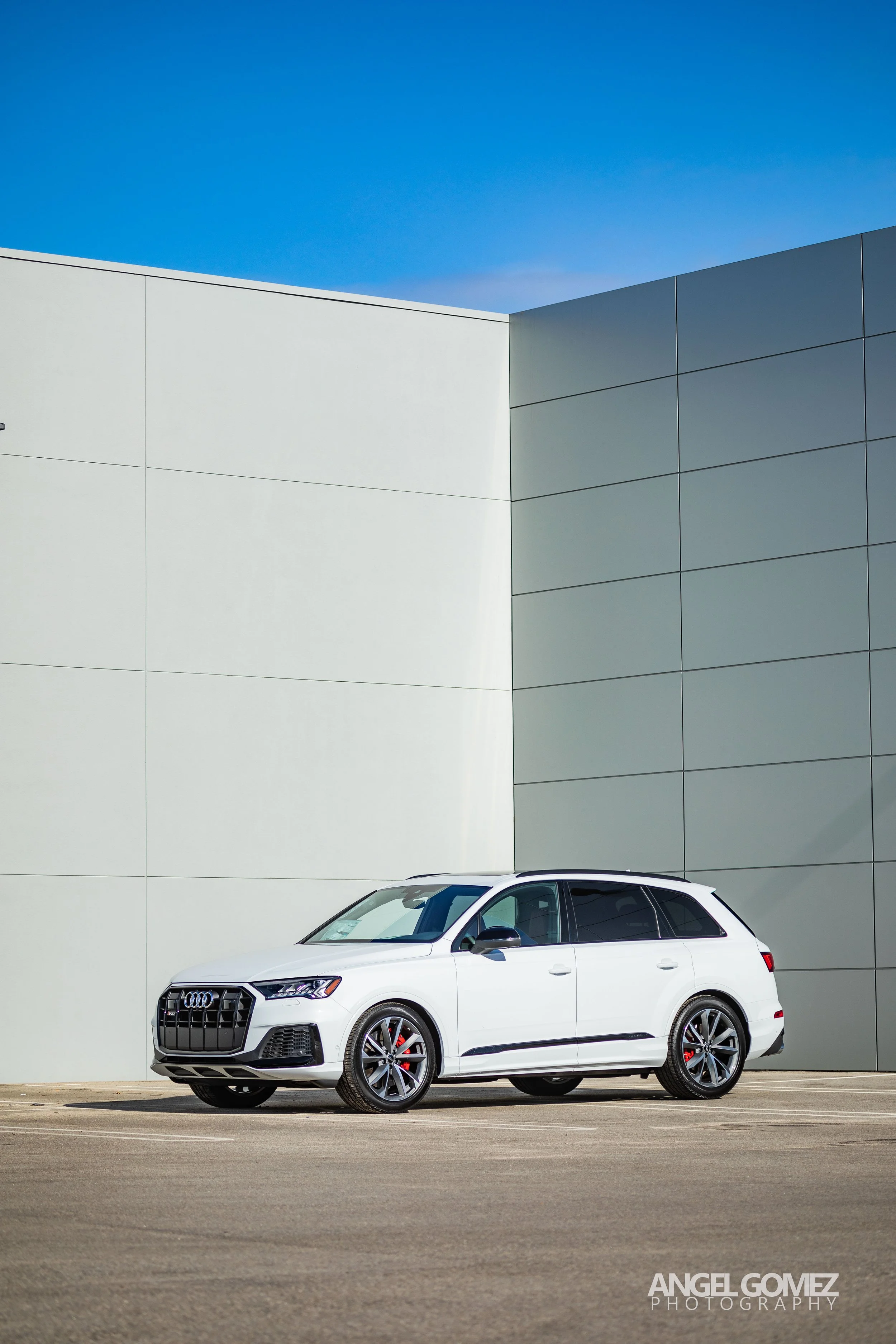 A white Audi station wagon parked in an empty lot against a modern white building with a blue sky background.