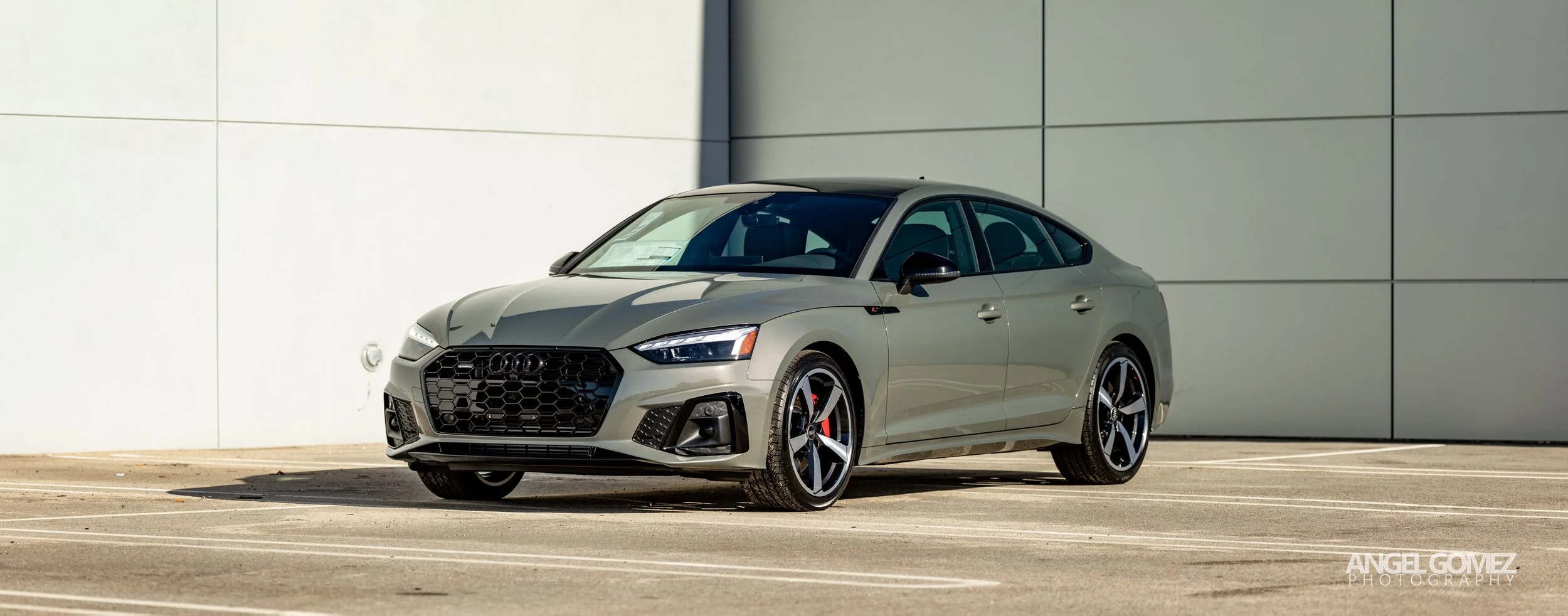 A silver Audi sedan parked outdoors in front of a modern building with a light-colored wall.
