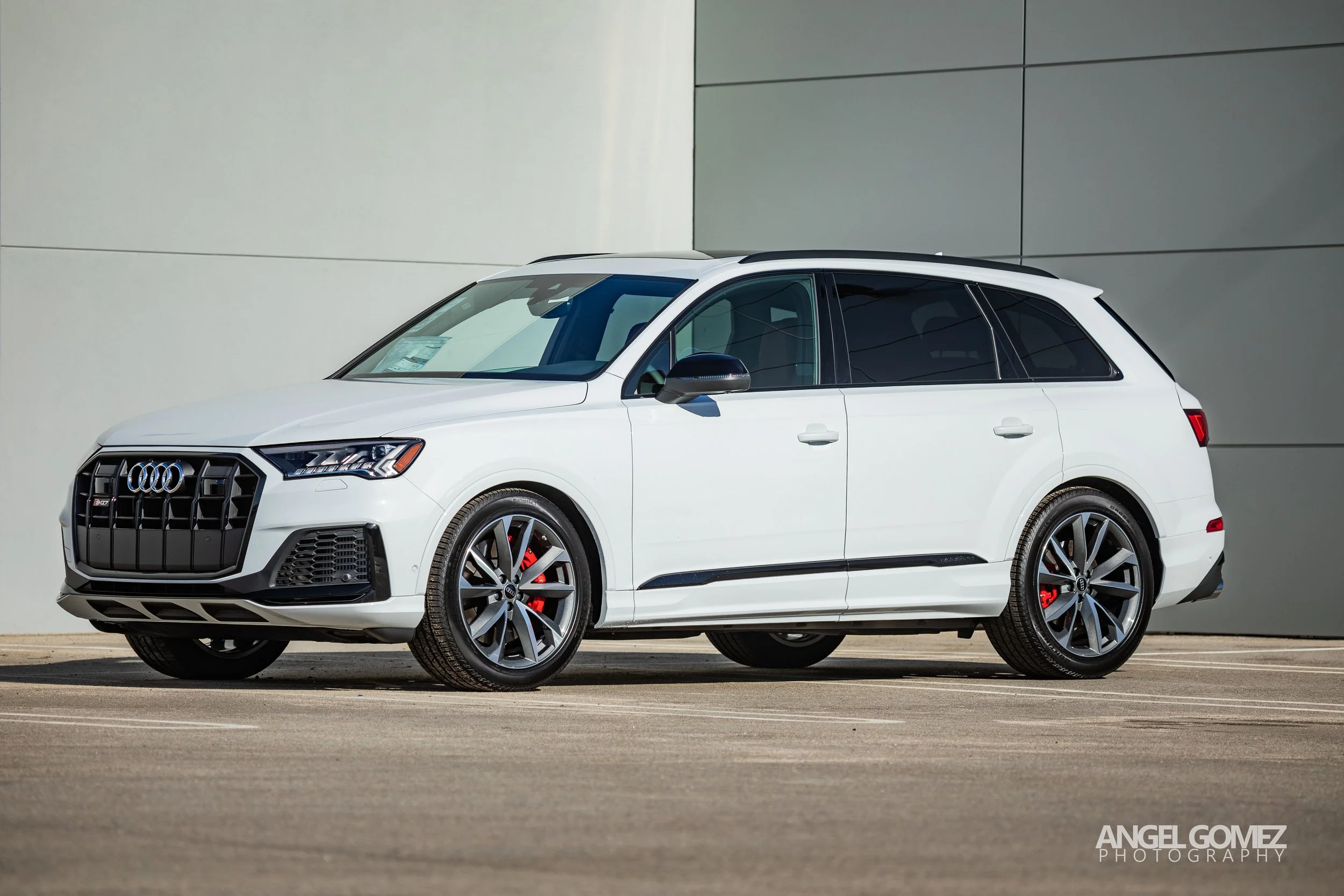 White Audi SUV parked on a paved surface against a modern gray wall.