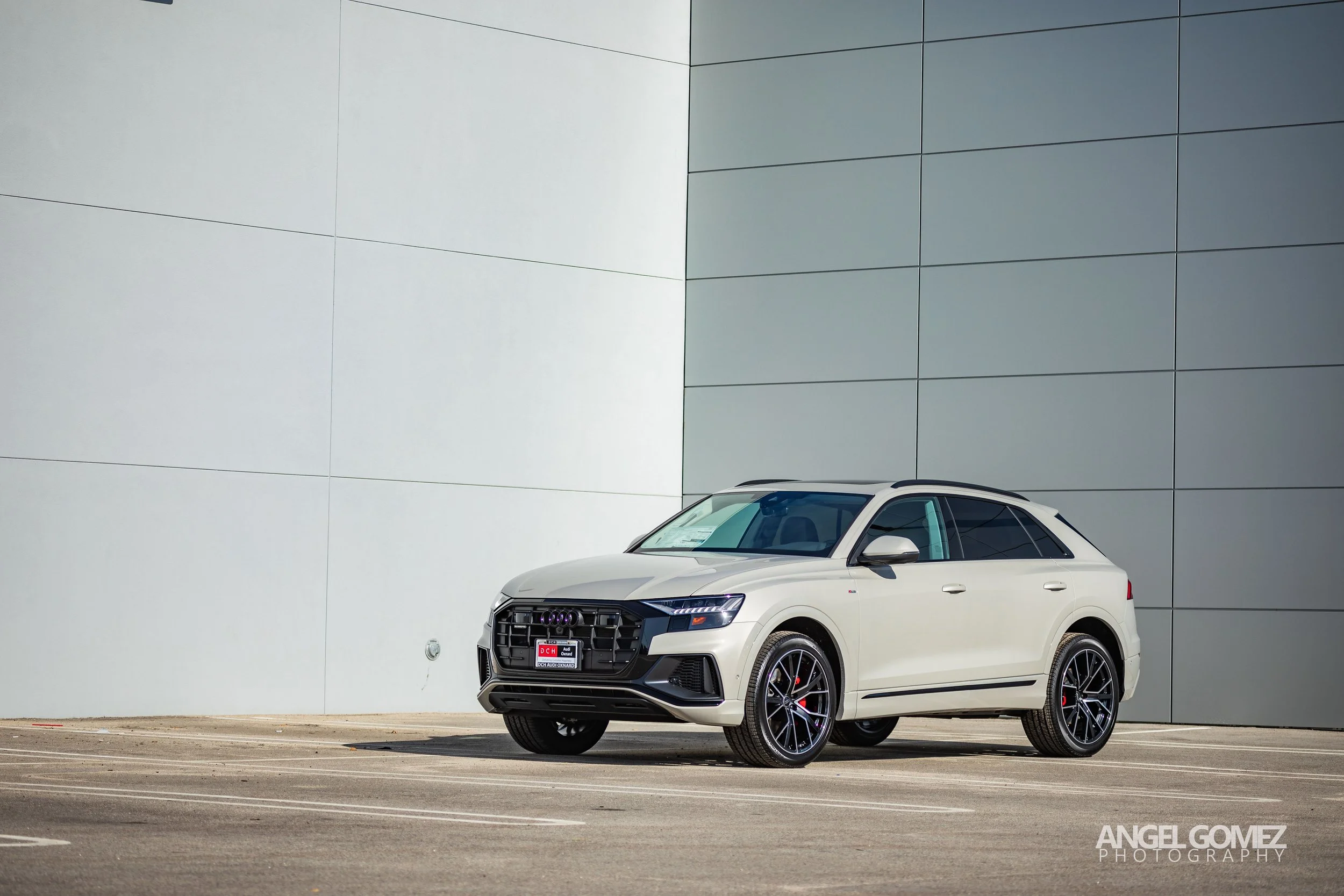 White Audi SUV parked in an empty parking lot against a modern, two-tone wall with white and gray panels.