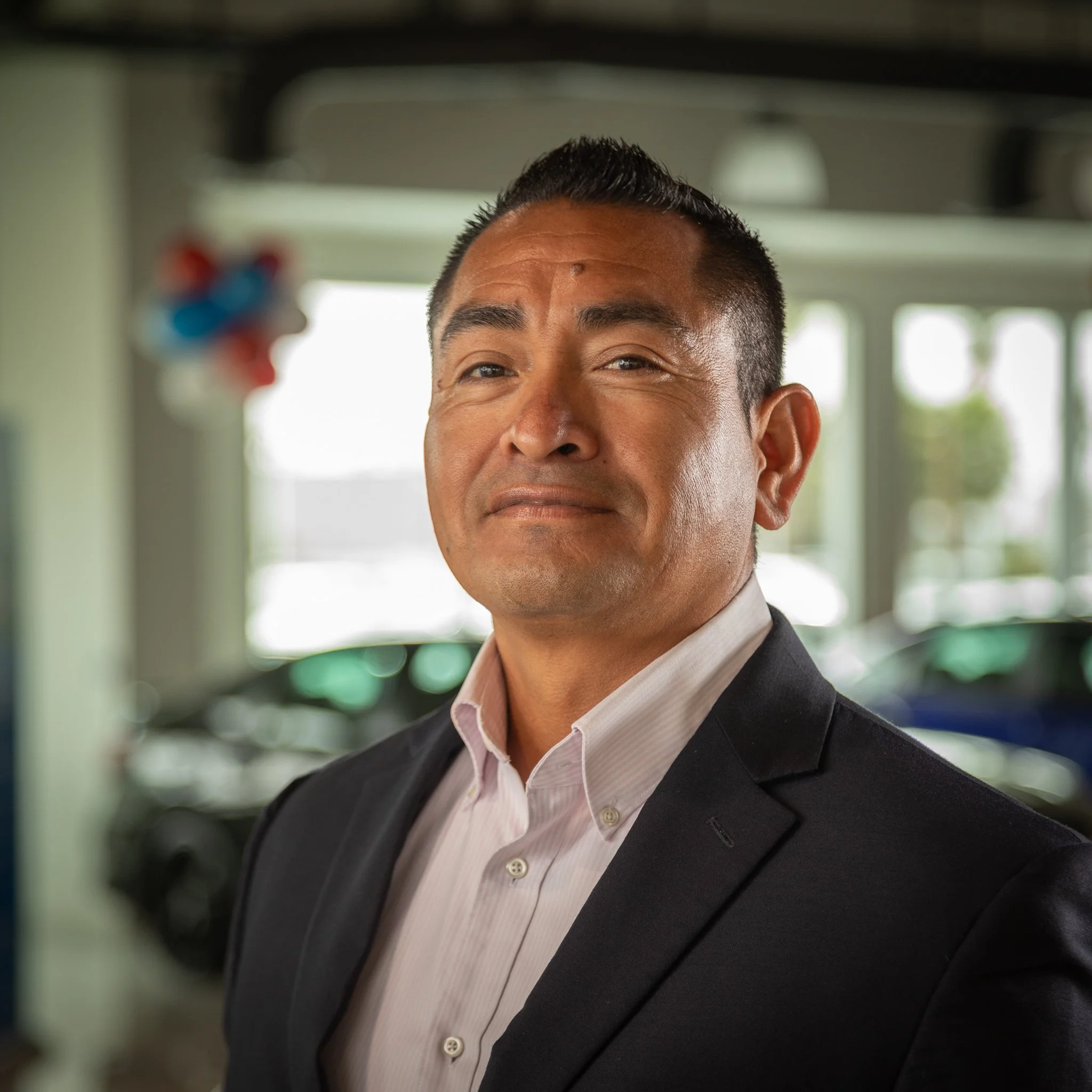 A confident middle-aged man in a suit at a car dealership.