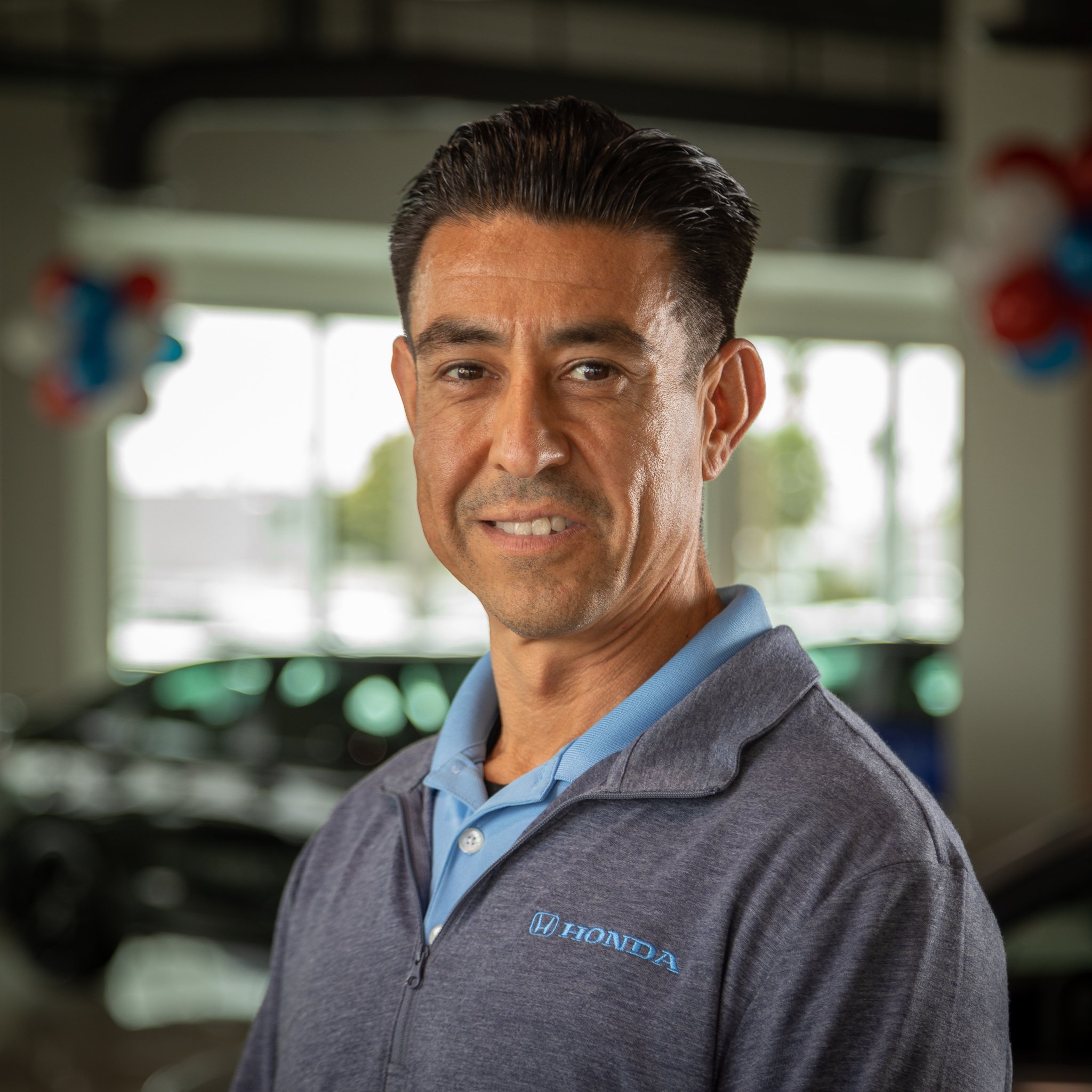 Man wearing a gray Honda jacket and blue polo shirt standing inside a car dealership.