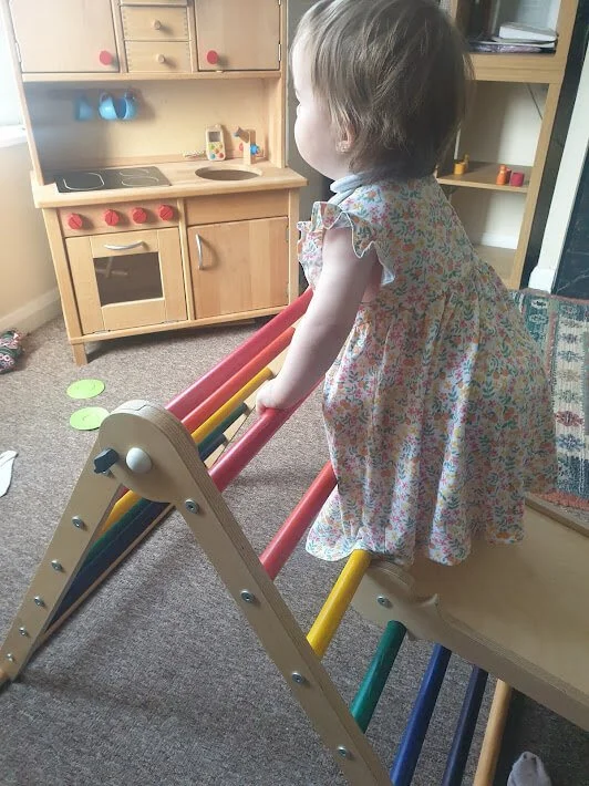 baby girl in dress climbing on wooden climbing frame