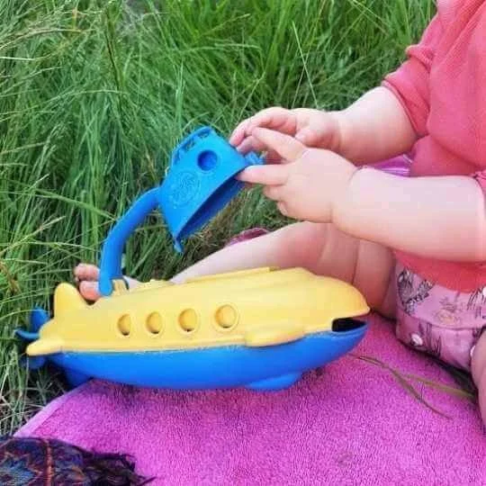 baby playing with green toys plastic toy submarine on grass