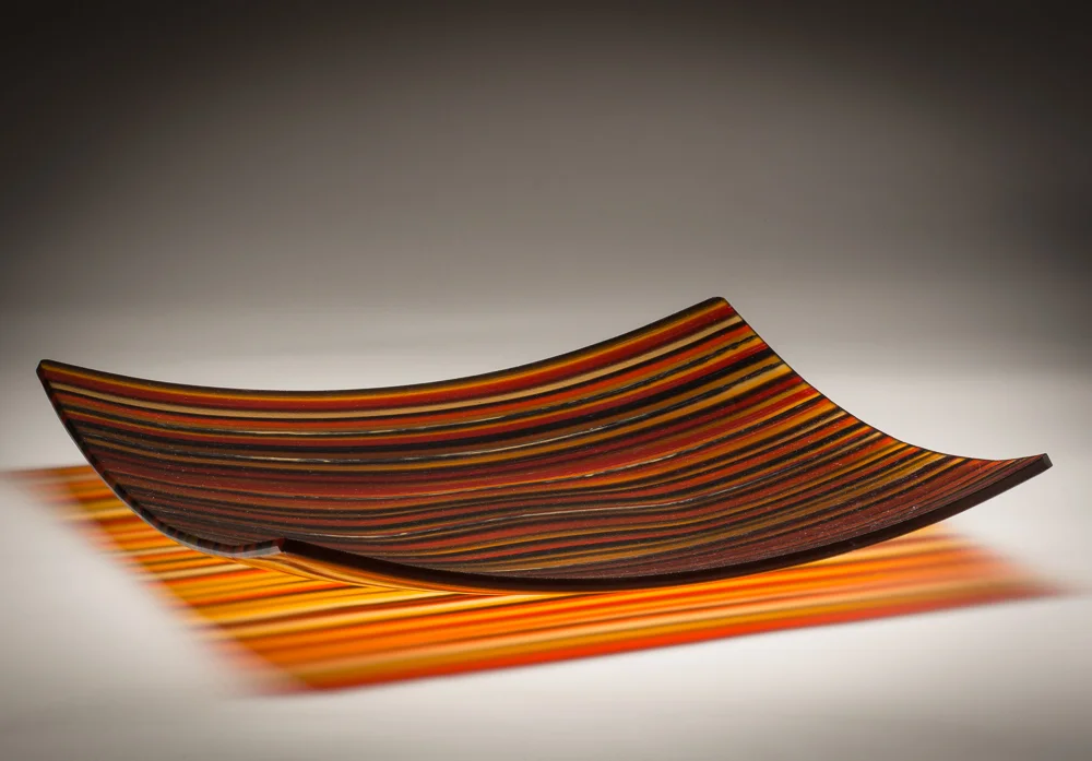 “Orange Delight” 14” X 14” Square Platter This piece began with sheet glass cut into 1/4” strips and placed on edge. It was fused in a kiln to combine all of the pieces to make one flat piece. It was put back into the kiln and “slumped” at a lower temperature on a mold. The glass takes the shape of the mold. This piece can be decorative, functional or both.