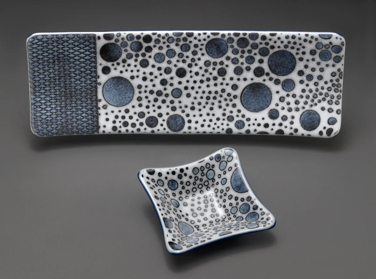“Shades of Grey” Rectangular Set This set started with 2 layers of sheet glass with white glass on top. The patterns were created using stencils an sifting glass powder over the the stencils. The pieces were then fired and the glass and glass powder became flat. Each piece was then put on a mold and “slumped” in the kiln at a glass warming temperature and the glass took the shape of the molds.