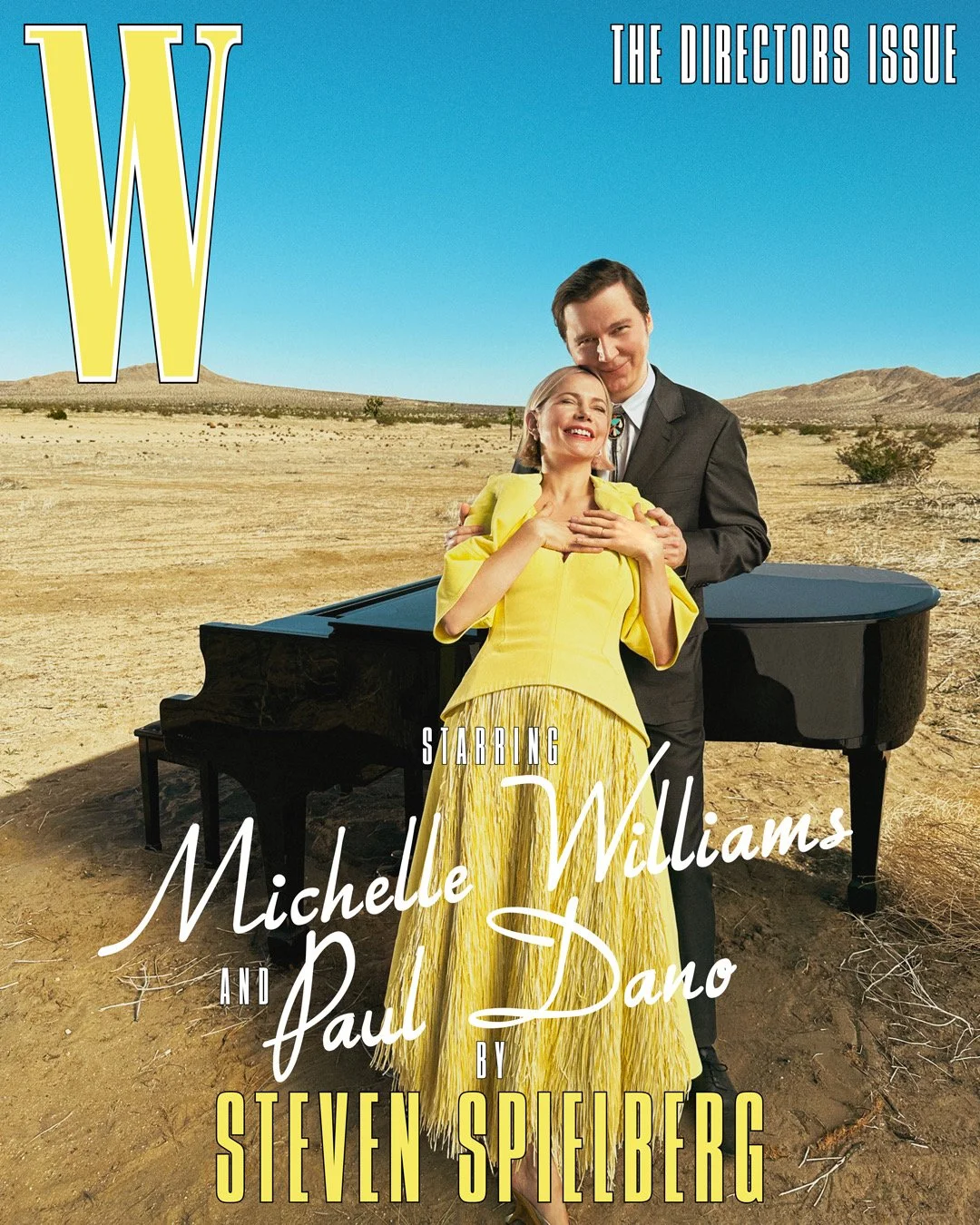 Cover of W magazine's 2023 director's issue featuring Michelle WIlliams and Paul Dano standing together beside a grand piano in teh California Desert. Michelle Williams wears a bright yellow dress and Paul Dano stands behimd her wearing a dark suit.
