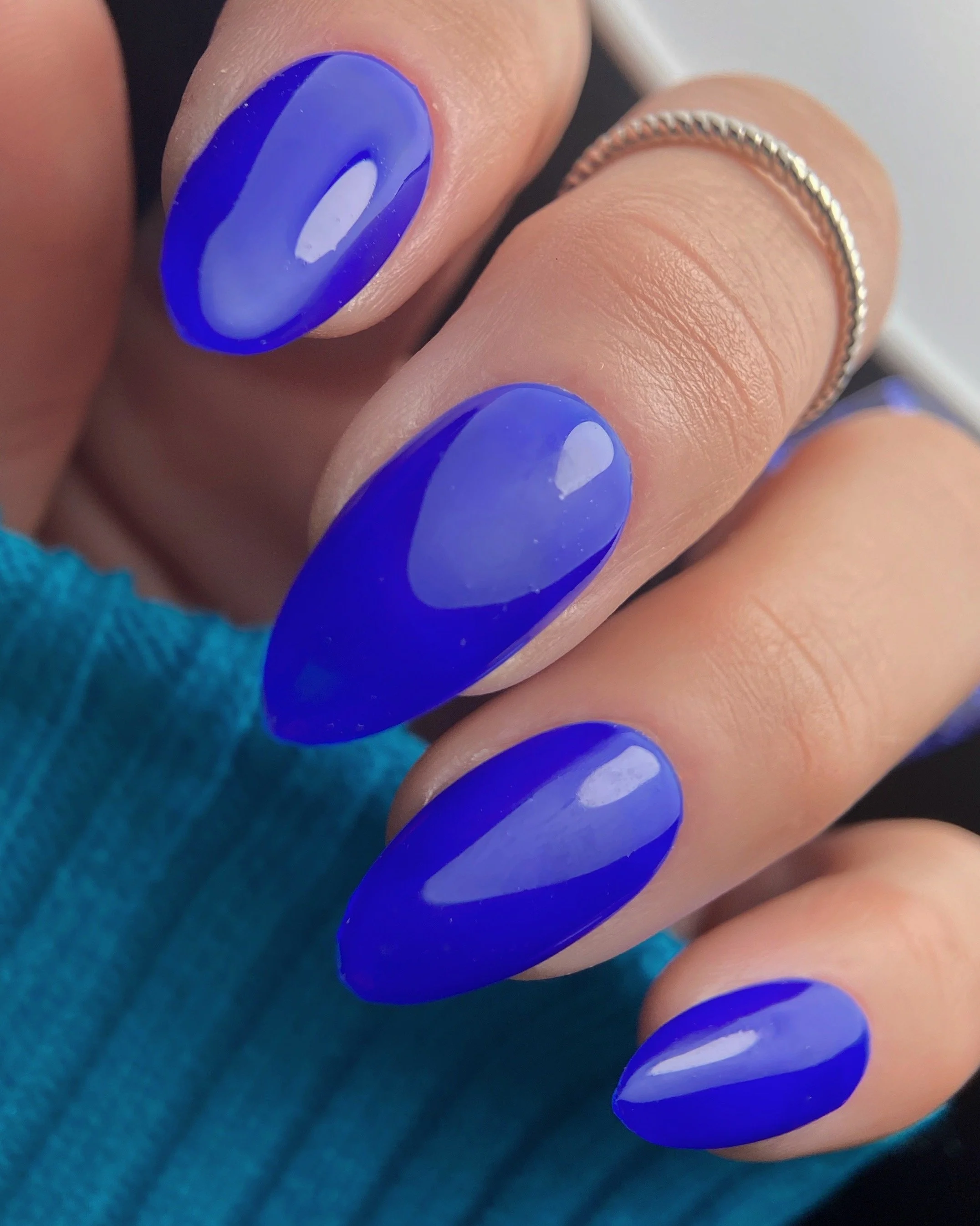 Nail Thoughts Celebration Collection gel color swatch in shade "LA Nights" a bright cobalt blue on manicured hand with rungs and knit sleeve.