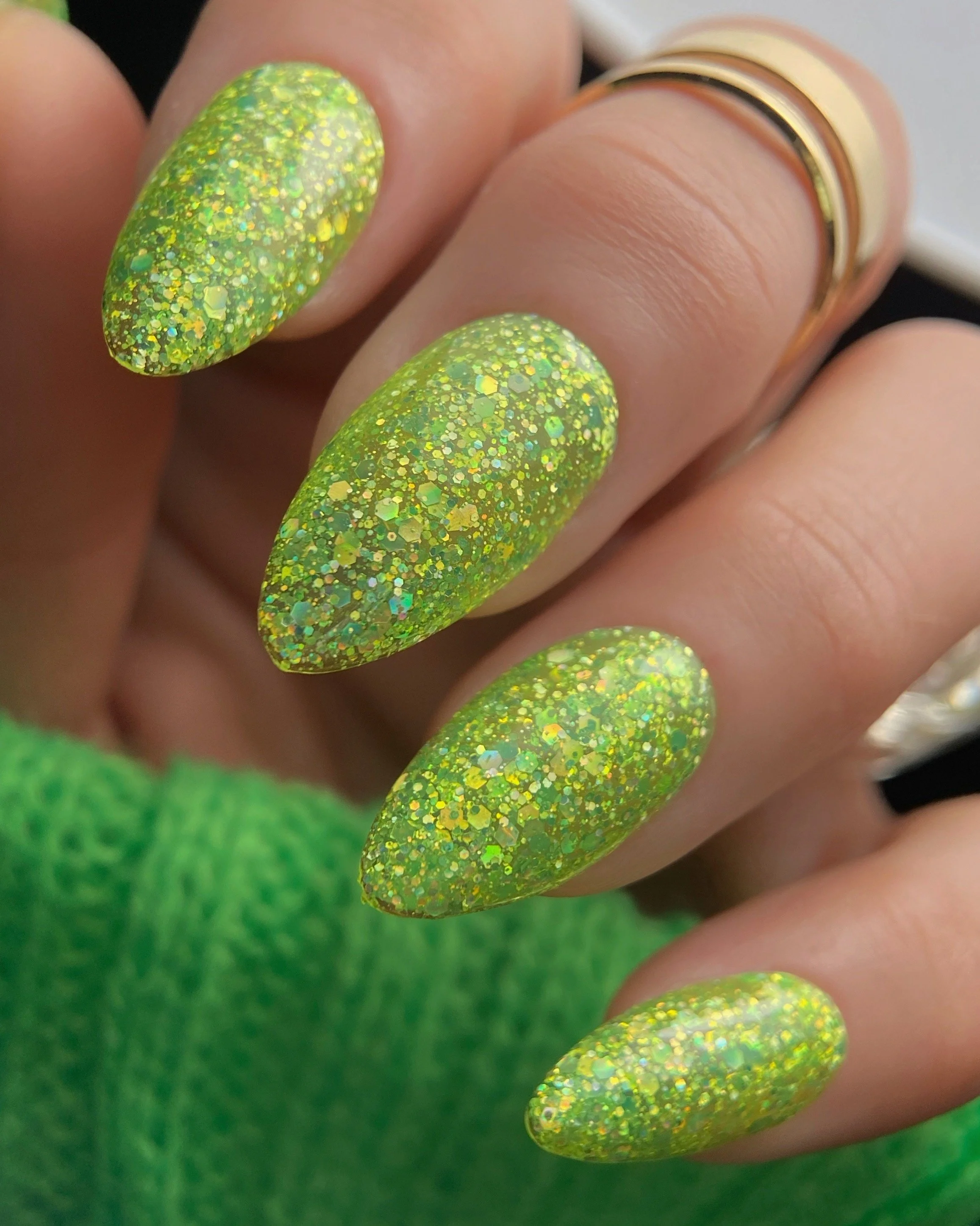 Nail Thoughts Celebration Collection gel color swatch in shade "Dancing Shoes" a bright lime chartreuse jelly glitter on manicured hand with rings and knit sleeve.