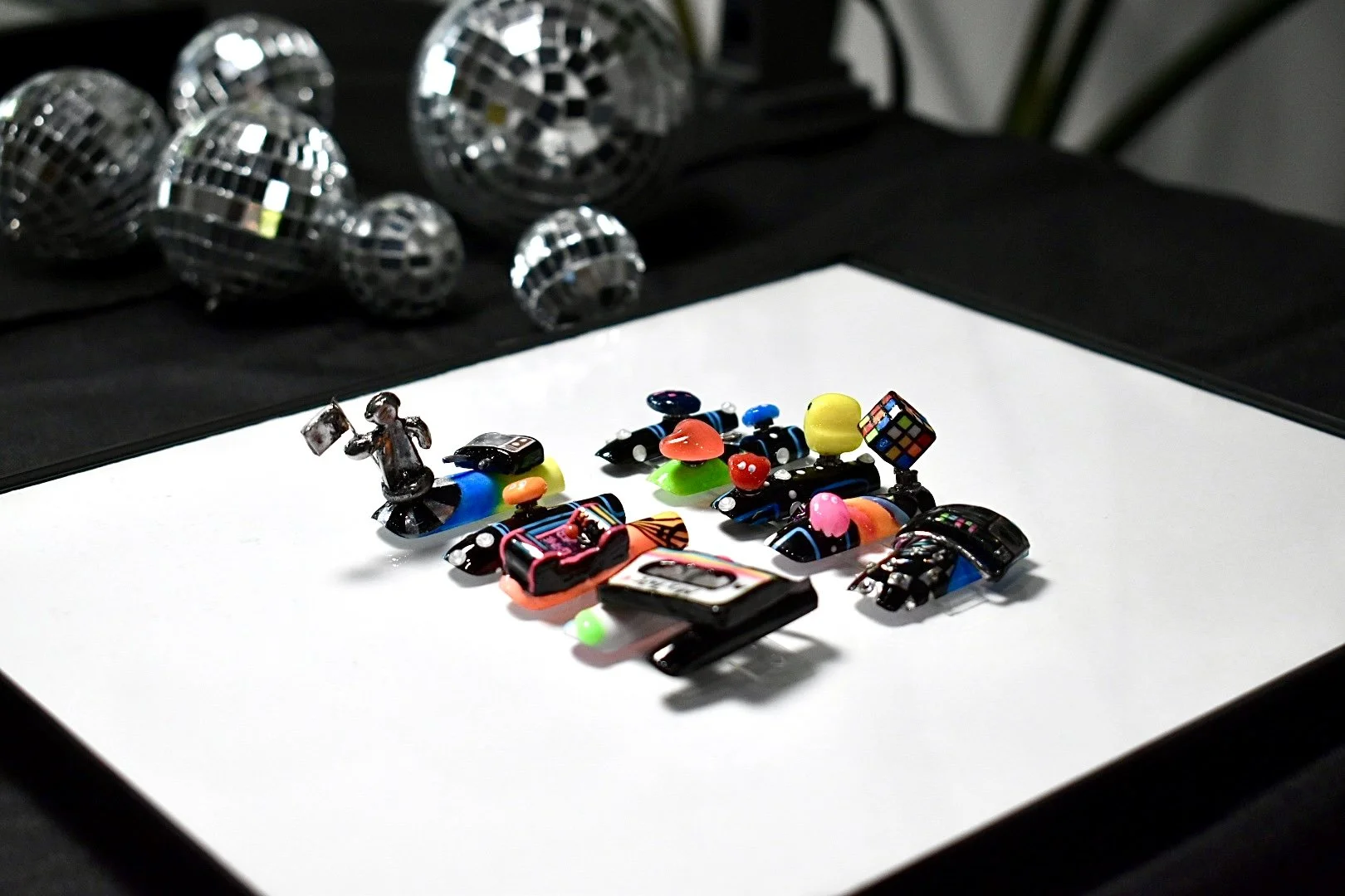 Totally '80s nail art competition entry at The Mani Mixer 2026 featuring miniature arcade-inspired sculptures, a Rubik's Cube, cassette player, and colorful geometric details.