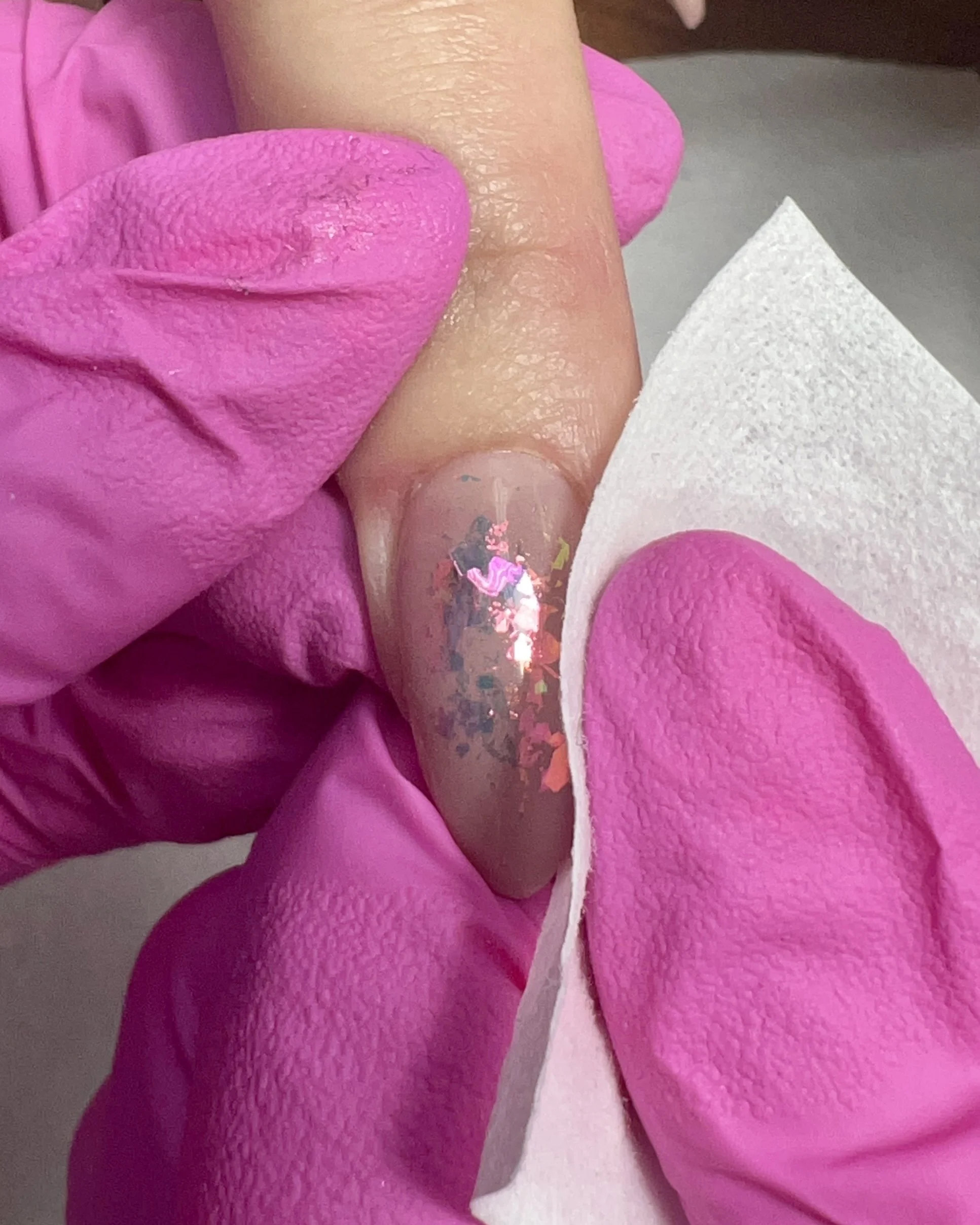 A lint-free wipe removes the inhibition layer from an encapsulated nail design, preparing the surface for chrome application.