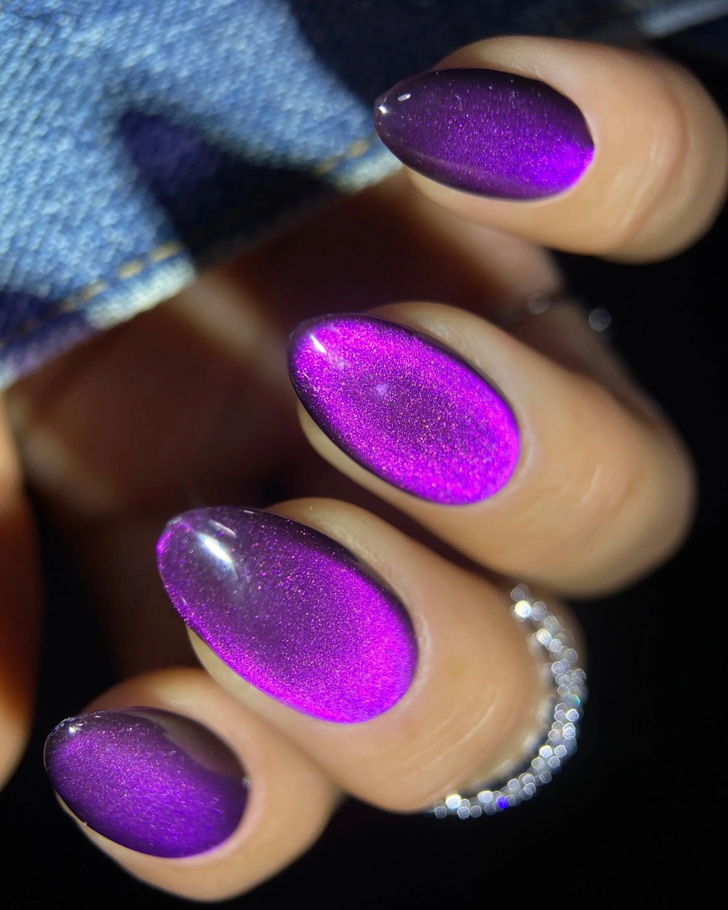 Close-up of Double Rhythm Gemstone Glow MC1325, a rich amethyst-purple magnet gel with a soft velvety magnetic effect and glossy finish on an almond-shaped nail tip photographed against denim.