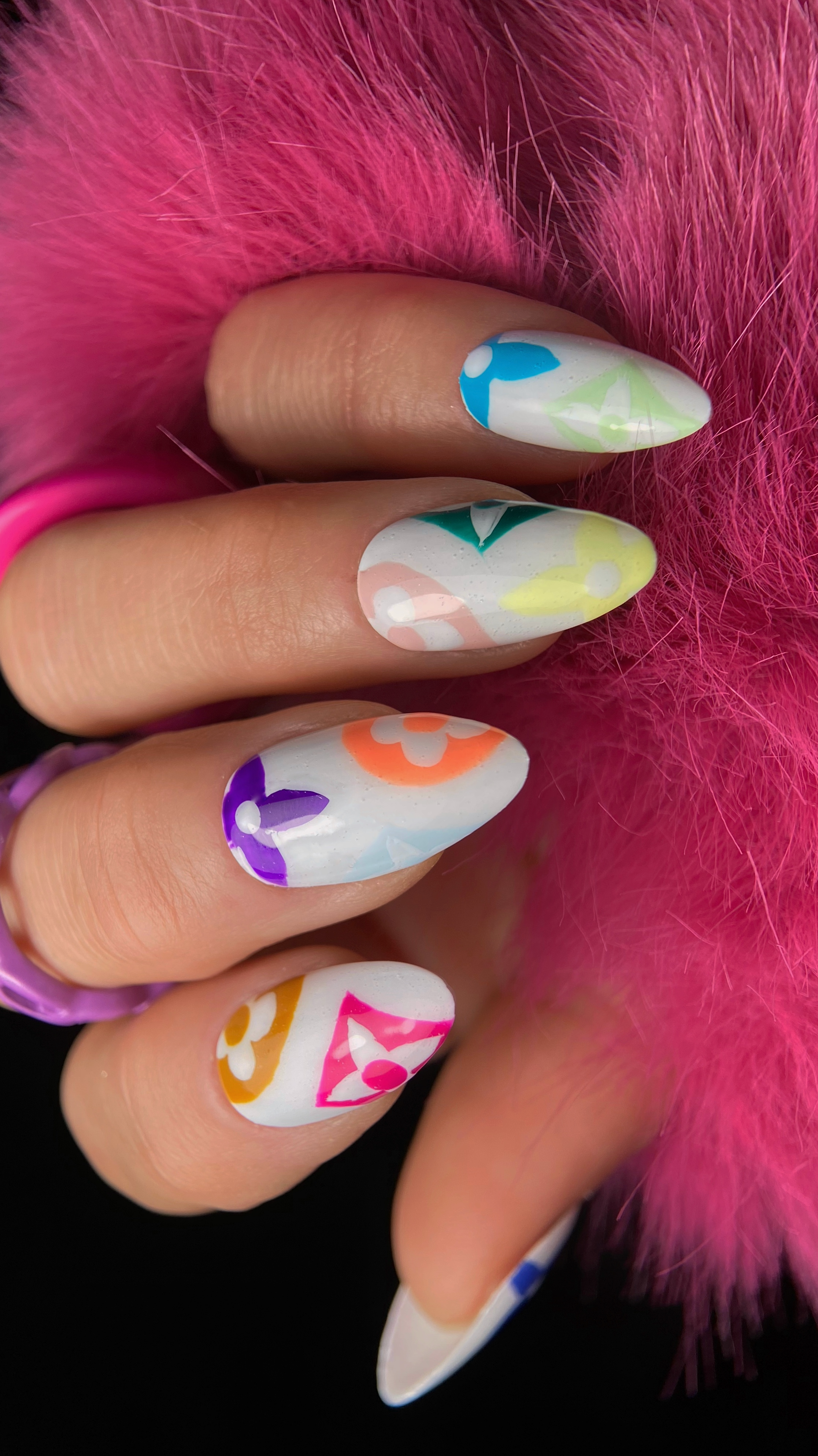 Almond-shaped nails featuring Louis Vuitton x Takashi Murakami inspired nail art with multicolored floral motifs, pink geometric accents, and vibrant blue, yellow, green, orange, and purple details painted over a white background.
