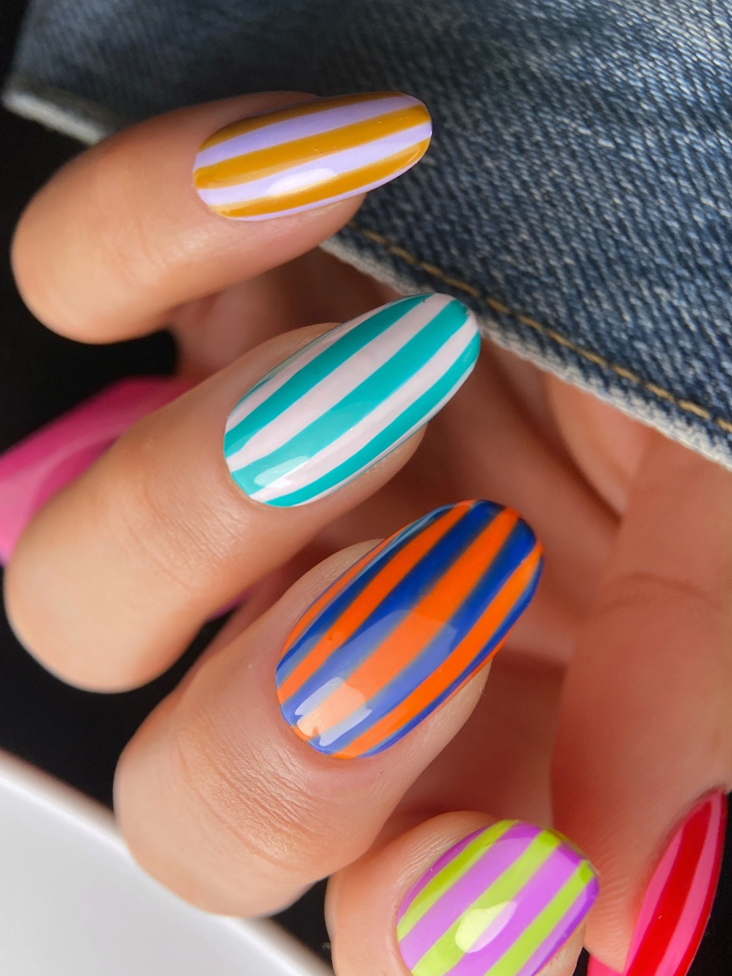 Close-up of colorful summer nail art featuring vertical stripes in orange and blue, turquoise and pale pink, lavender and mustard and lime green and purple.