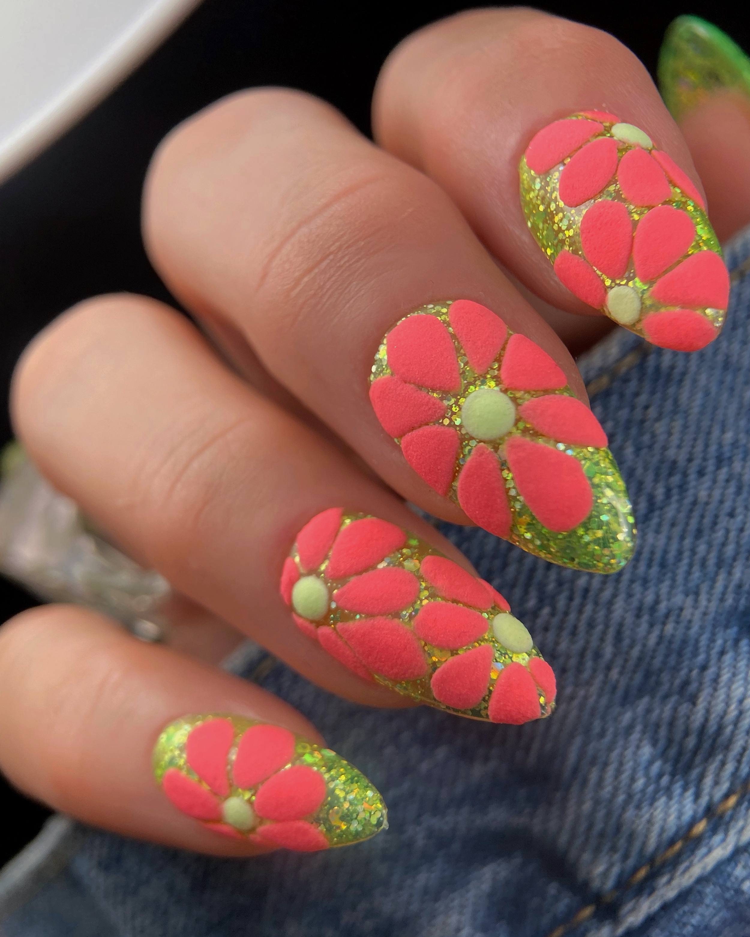 Puff paint flower nail art featuring raised neon pink flowers with pale green centers over a glittery chartreuse gel base on almond-shaped nails.