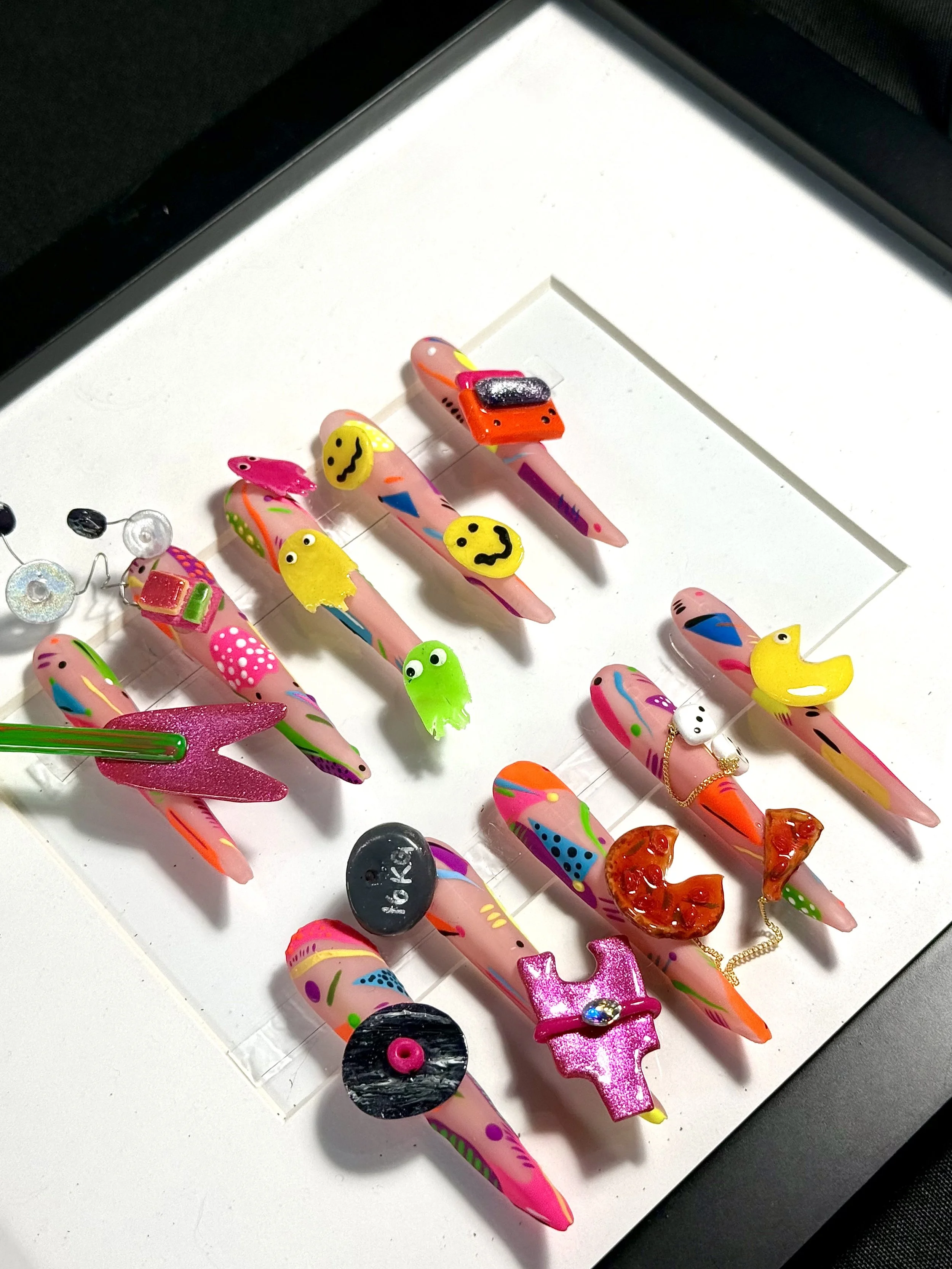 Totally '80s nail art competition entry at The Mani Mixer 2026 featuring sculptural smiley faces, Pac-Man ghosts, cassette tape, vinyl record, pizza slices, roller skate, rubber duck, and colorful abstract nail art.