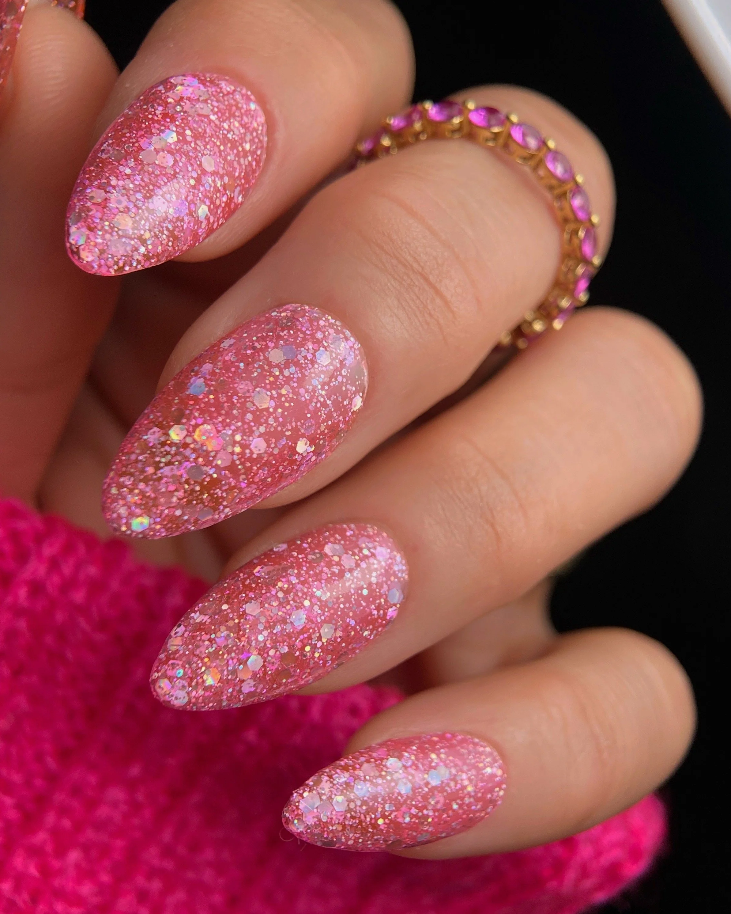 Nail Thoughts Celebration Collecion "Matsuri" pink glitter gel swatch on manicured hand with rings in pink knit sleeve.