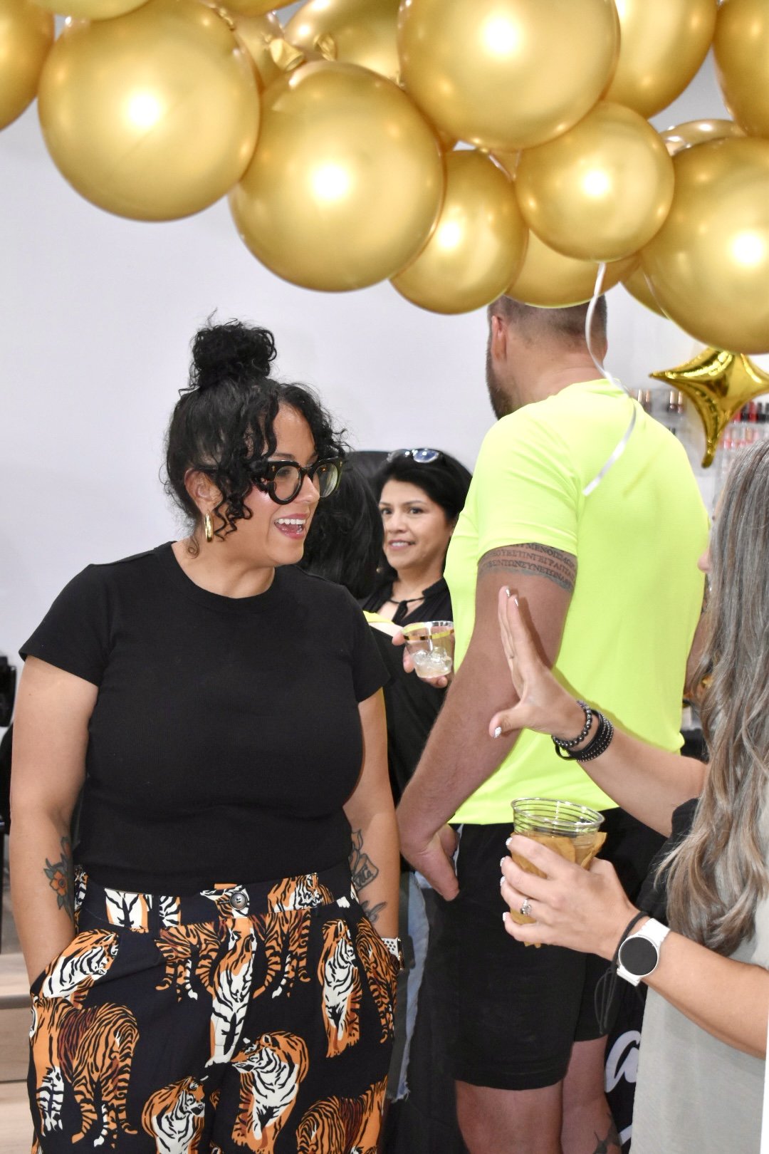 Rachel Messick talking with an attendee during The Mani Mixer 2026 while attendees network beneath gold balloon decorations.
