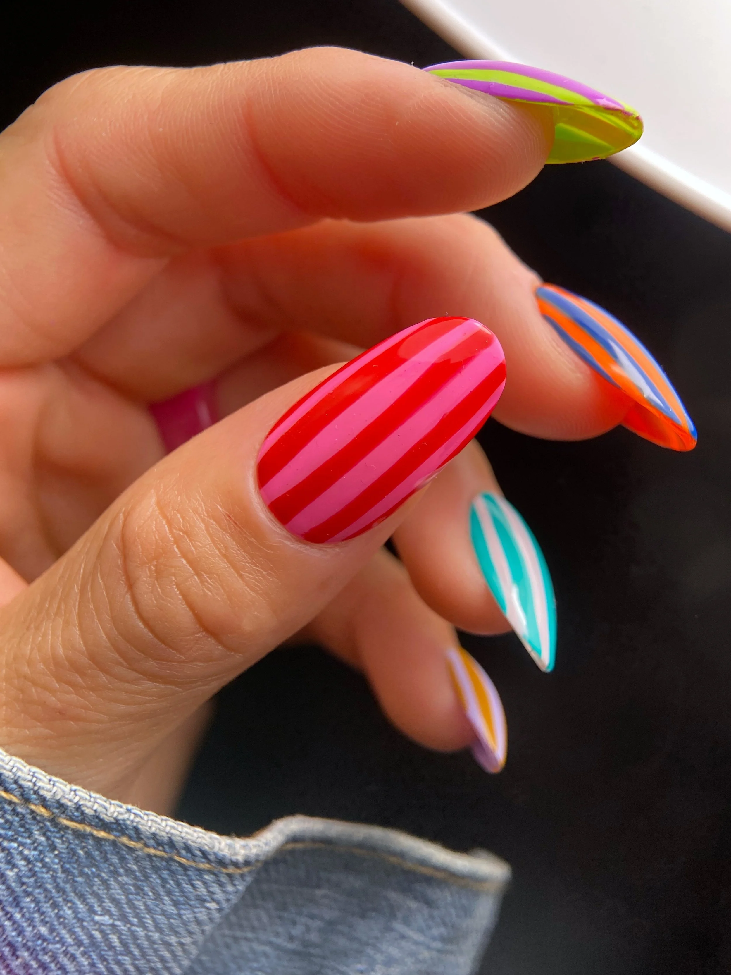 Colorful vertical striped nail art in bright summer color combinations including red and pink, orange and blue, turquoise and pale pink, lime green and purple and lavender and mustard.
