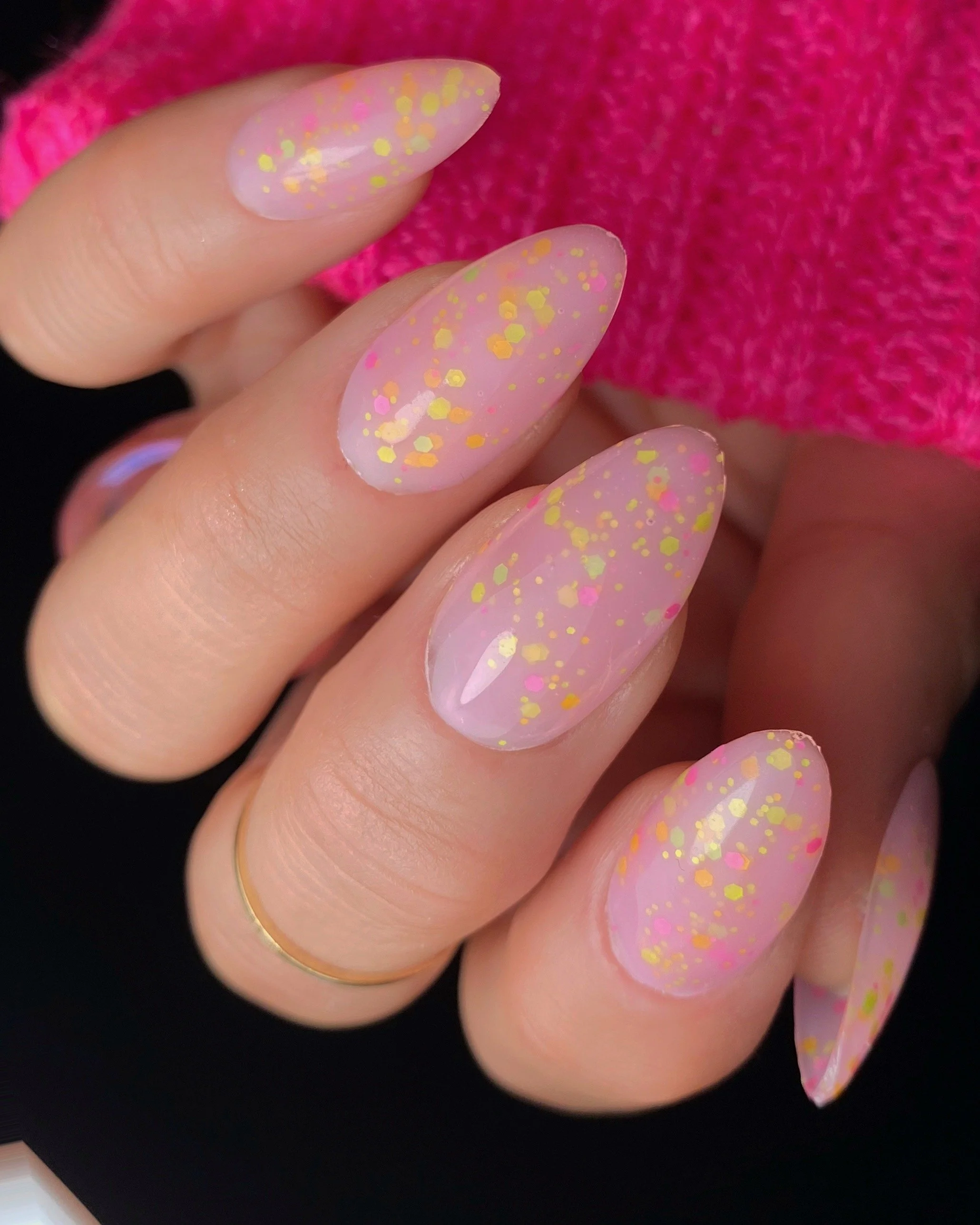Nail Thoughts Celebration Collection gel color swatch in shade "It's My Bday" a sheer nude pink with satin confetti glitter on manicured hand with rings and knitted pink sleeve.
