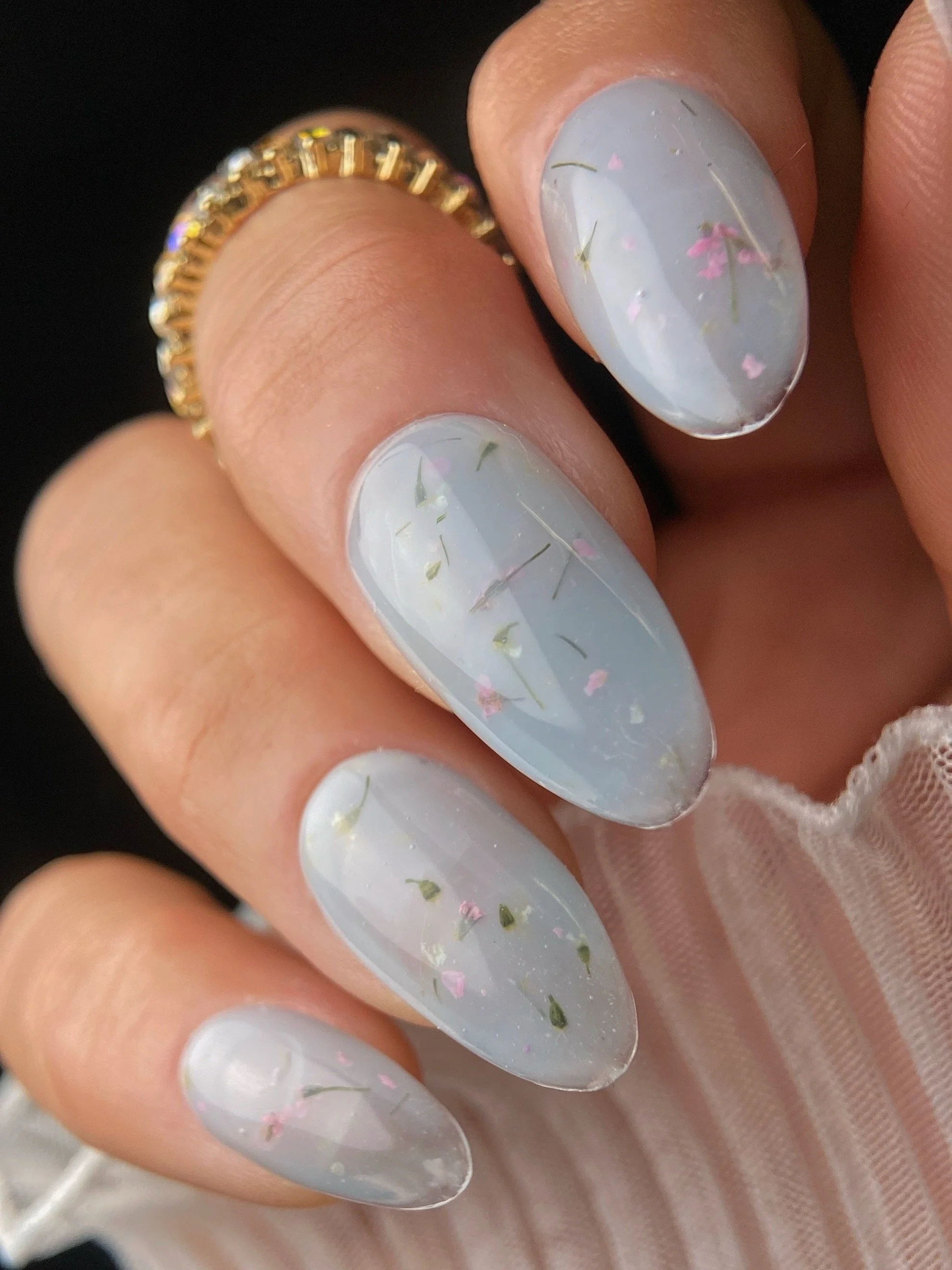 KOKOIST Botanical Flower Gel BF-01 Milky Blue swatch with delicate pink flowers and green botanical pieces in a translucent milky blue base.