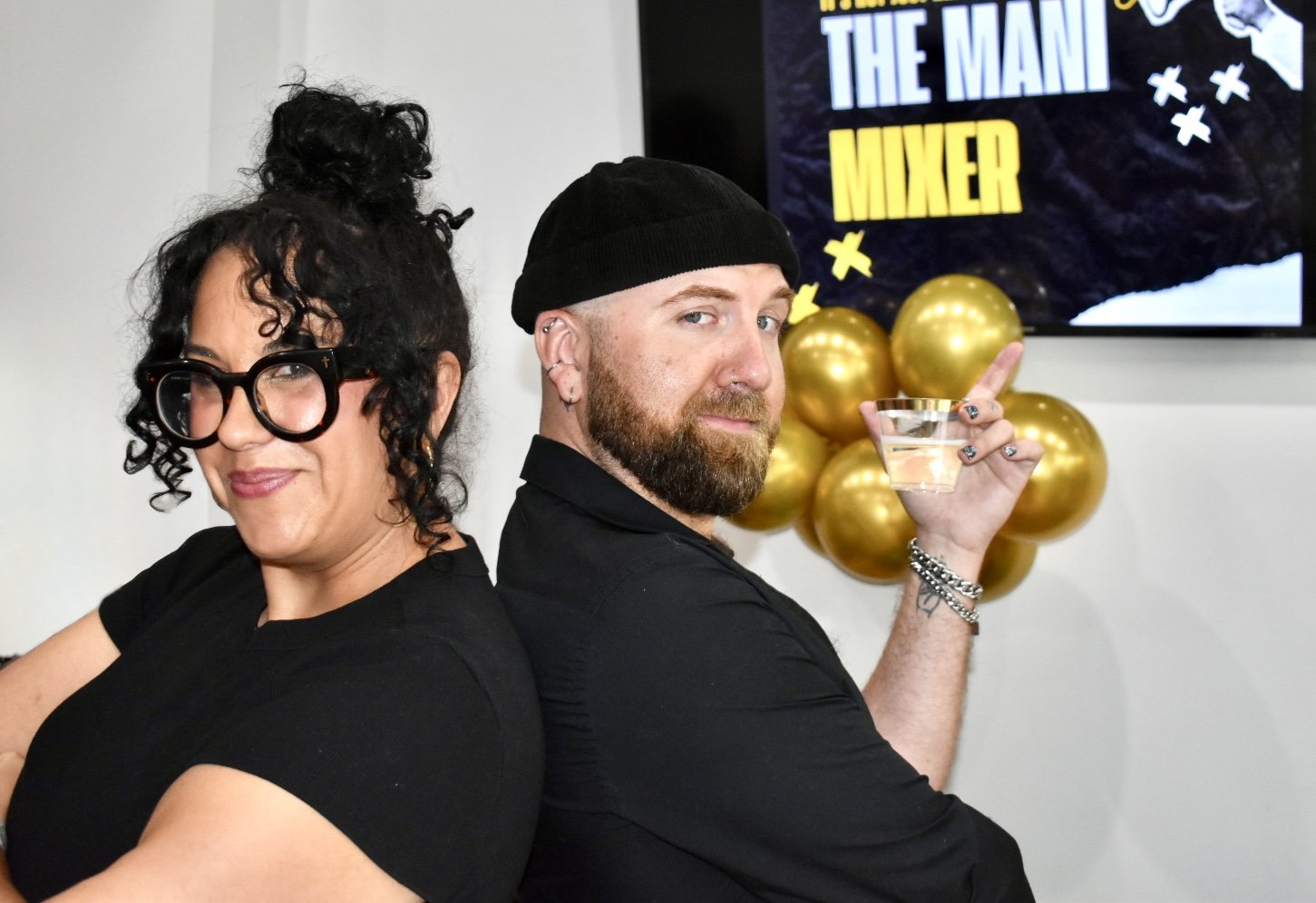 Rachel Messick and Dylan Pritchard posing back-to-back in front of The Mani Mixer 2026 event signage.