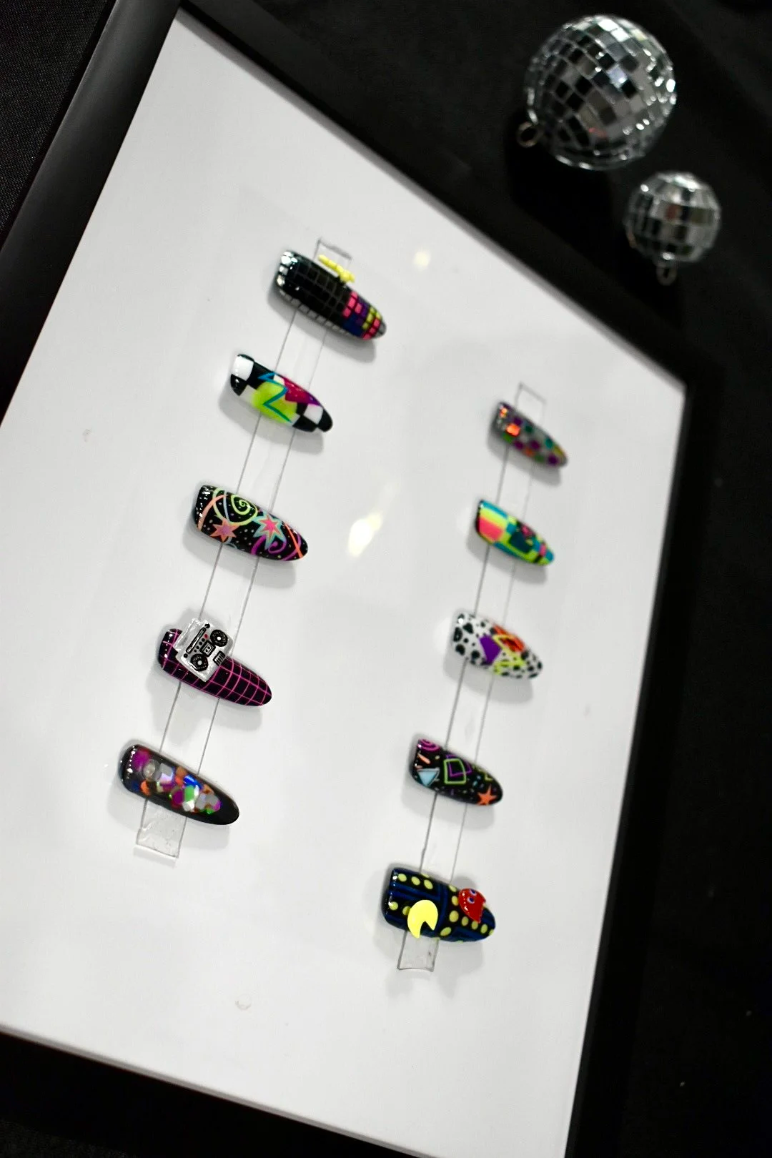Totally '80s nail art competition entry at The Mani Mixer 2026 featuring hand-painted neon nail art with Memphis-inspired geometric patterns, cassette tape, boombox, checkerboard design, Pac-Man, and holographic glitter accents.