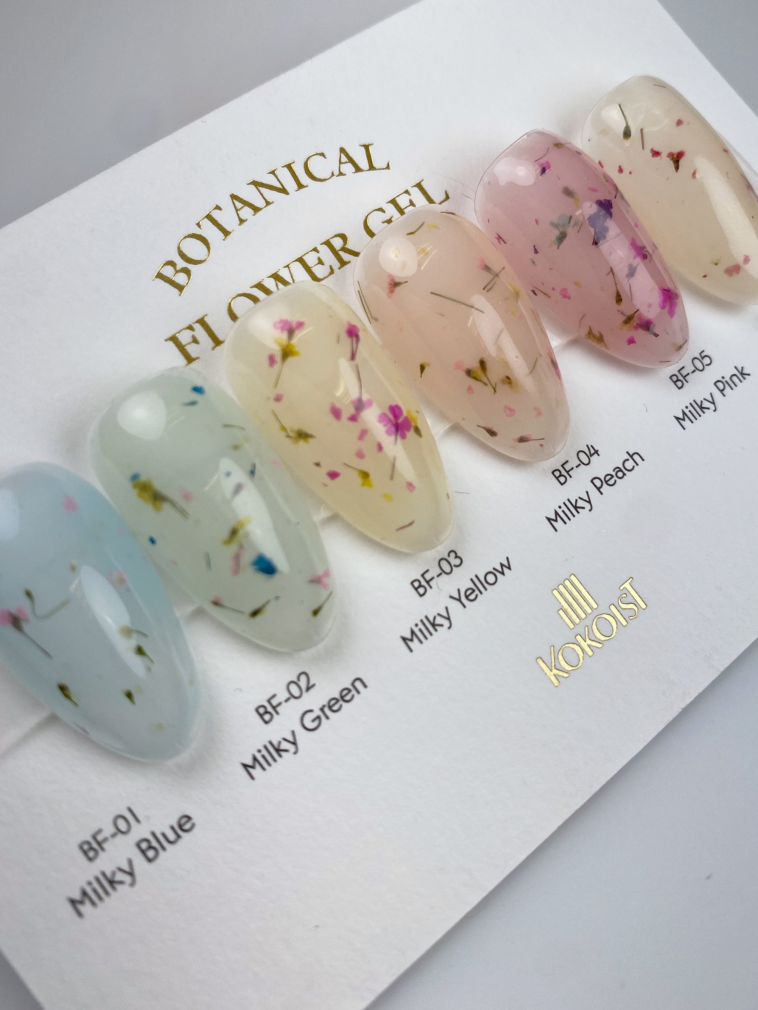 KOKOIST Botanical Flower Gel swatches in BF-01 Milky Blue, BF-02 Milky Green, BF-03 Milky Yellow, BF-04 Milky Peach, BF-05 Milky Pink and BF-06 Milky Beige, featuring sheer pastel gels with colorful dried flowers.