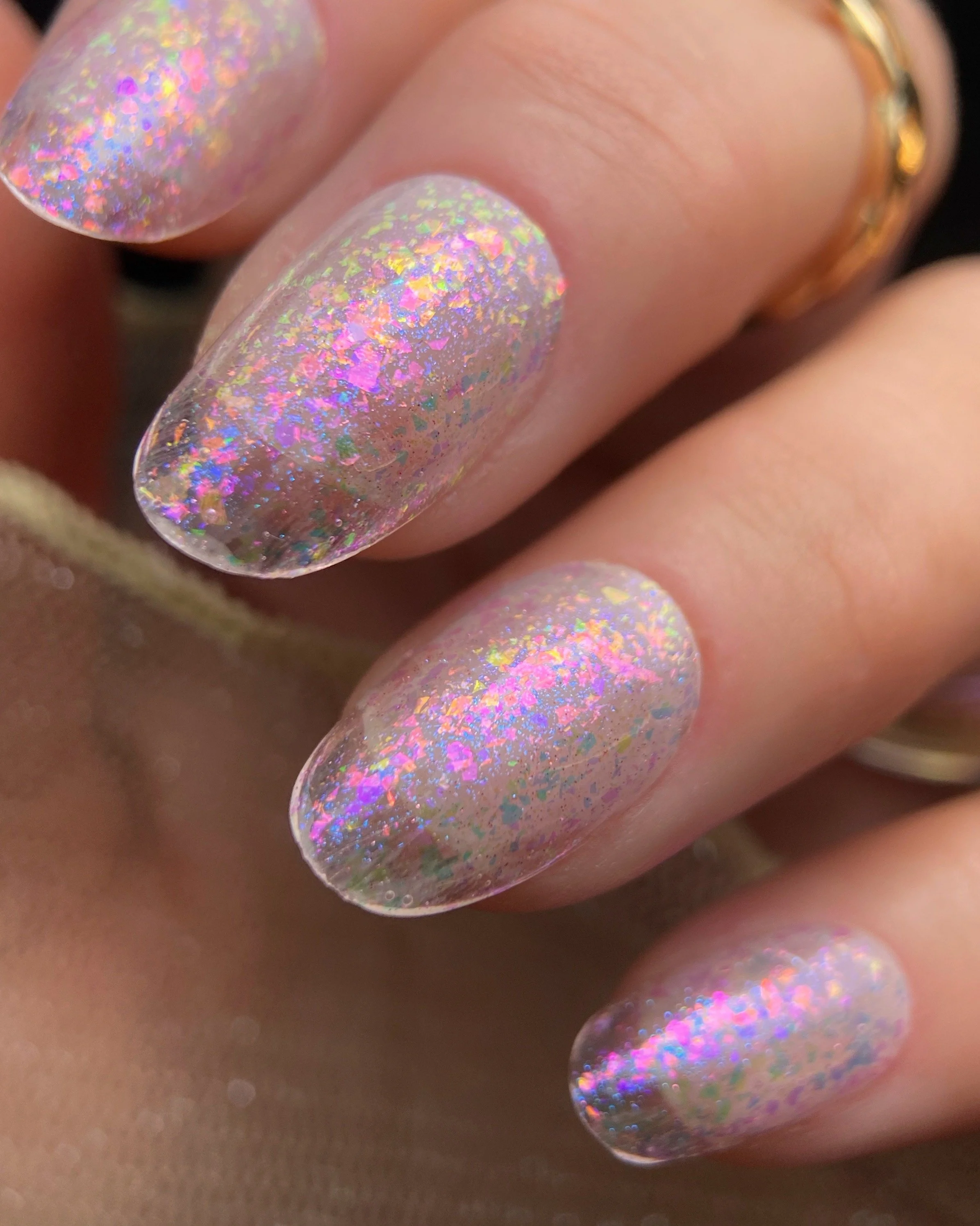 Close-up swatch of Orly Pink Moon glitter nail polish on oval shaped nails featuring iridescent pink, purple, and blue reflective flakes.