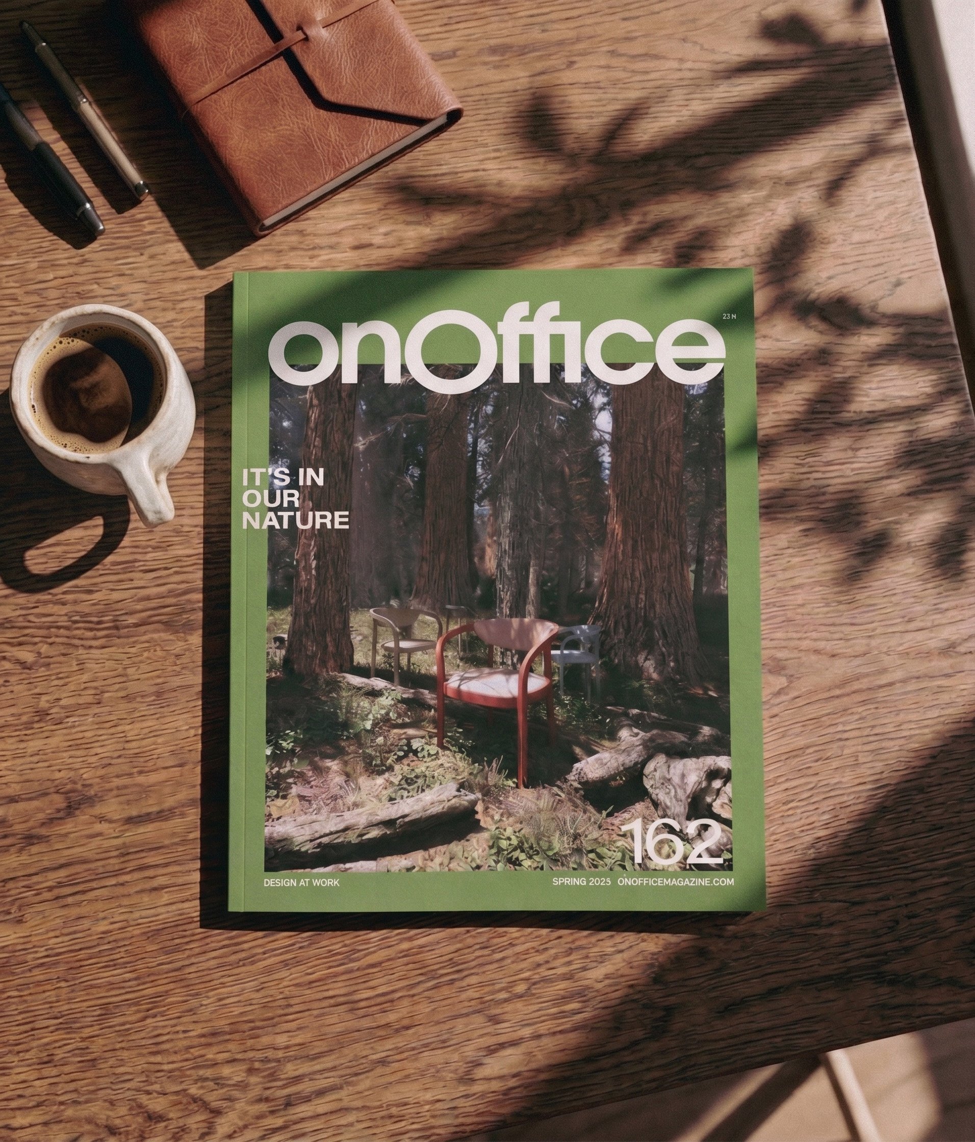 A magazine titled 'onoff' placed on a wooden surface next to a coffee mug and some pens with a brown leather notebook in the background. The magazine cover features a forest scene with large trees.