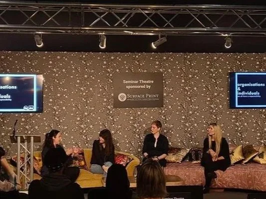 Panel discussion with four women on stage at seminar theater, with audience members viewing.