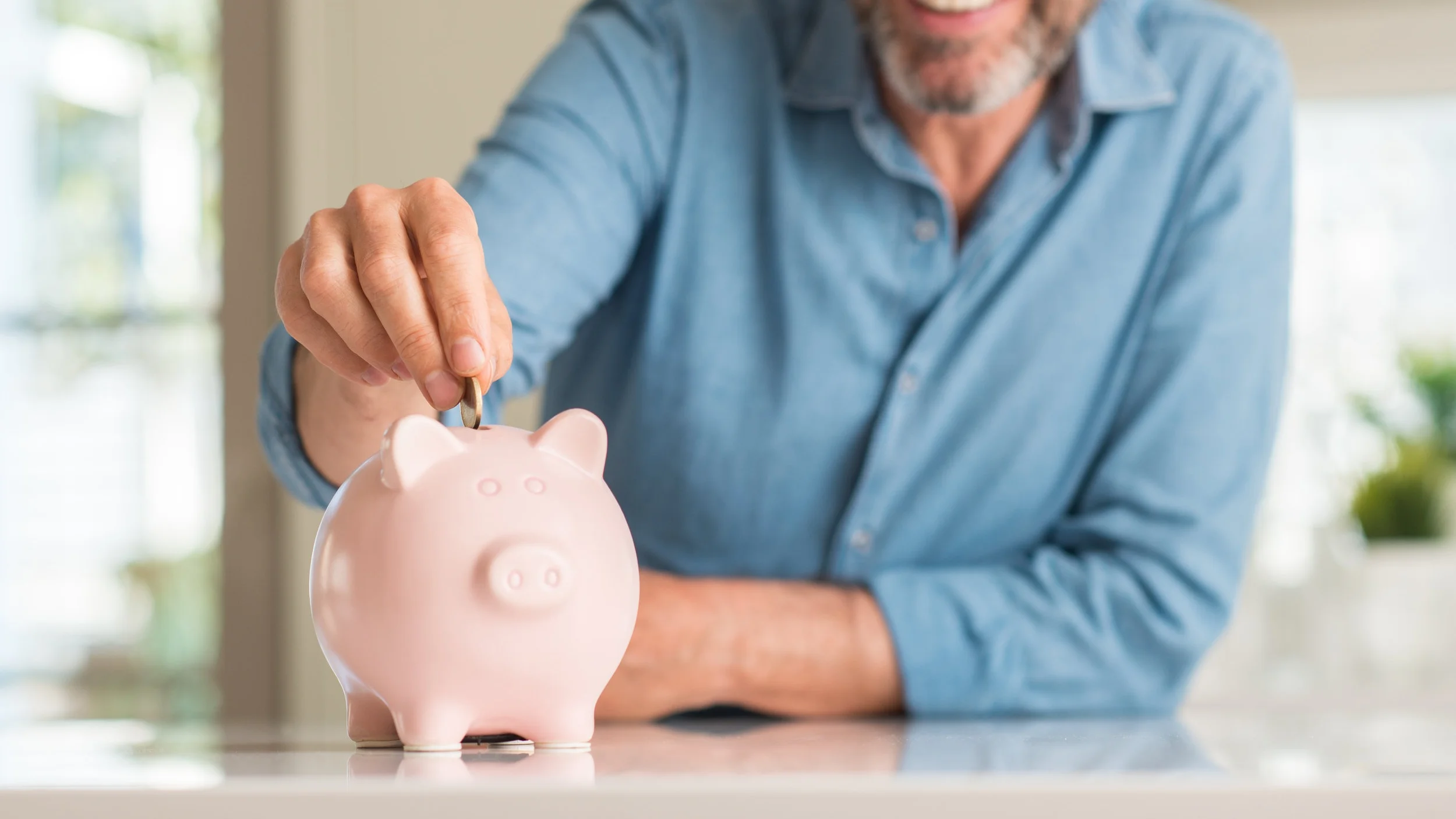 Middle age man save money on piggy bank with a happy face standing and smiling with a confident smile showing teeth